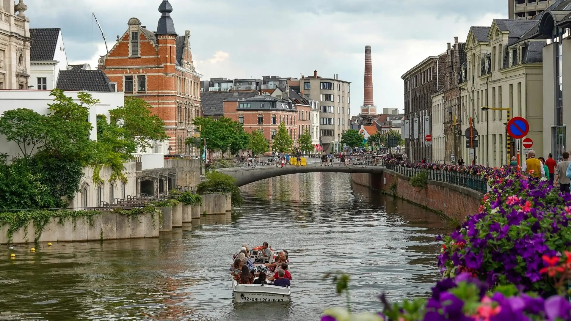 Fluss mit Booten und historischen Giebelhäusern am Ufer in Gent bei Sonnenuntergang.