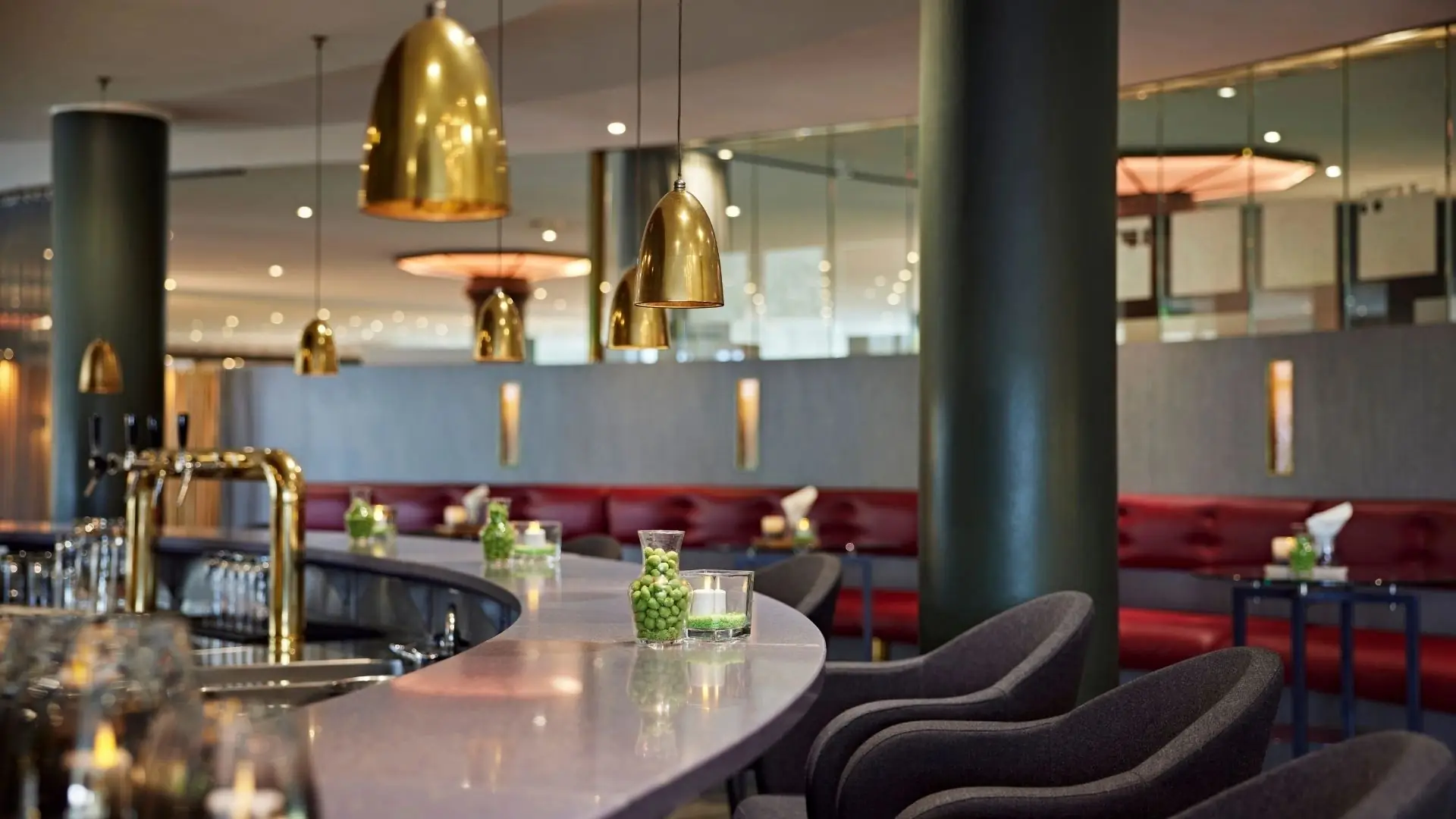 Geschwungene Bar mit goldfarbenen Hängeleuchten, schwarzen Säulen und dunkelgrauen Barhockern im Golf & Sporthotel Wiesensee