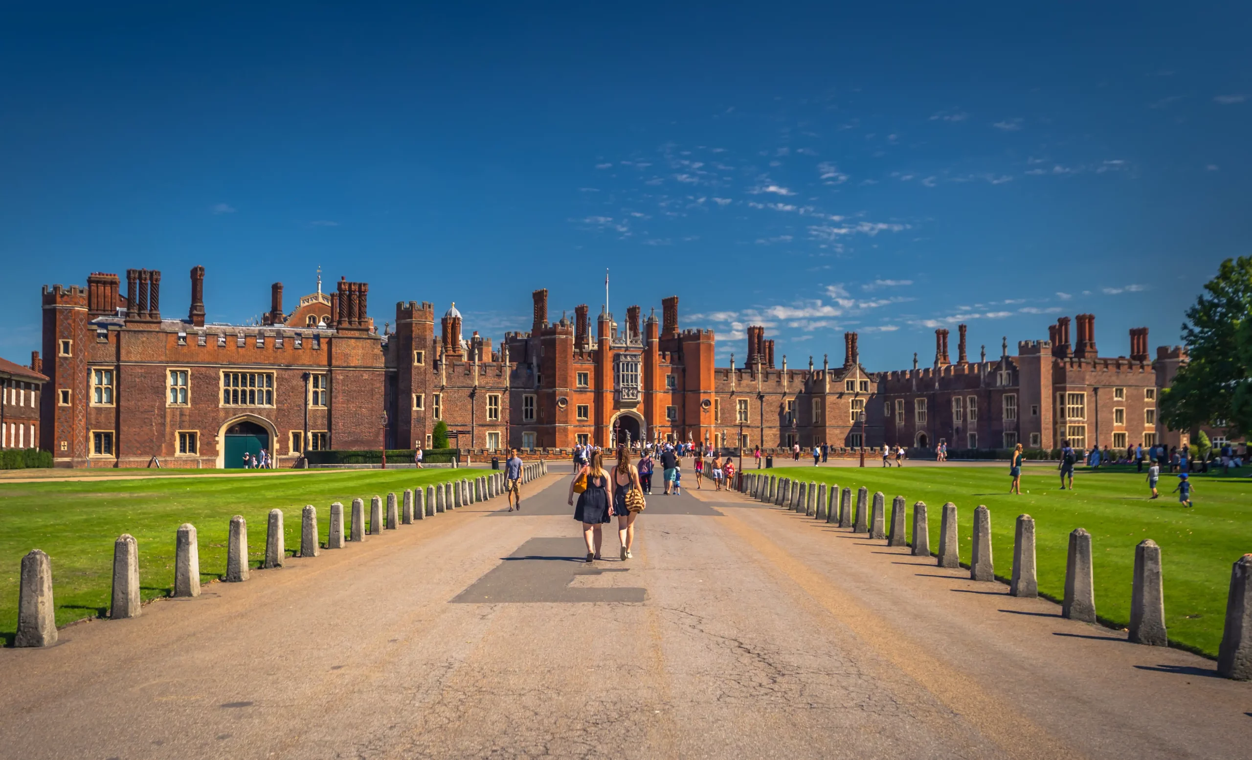 Besucher strömen bei sommerlichen Wetter auf den Haupteingang des Hampton Court Palace in London, England zu.