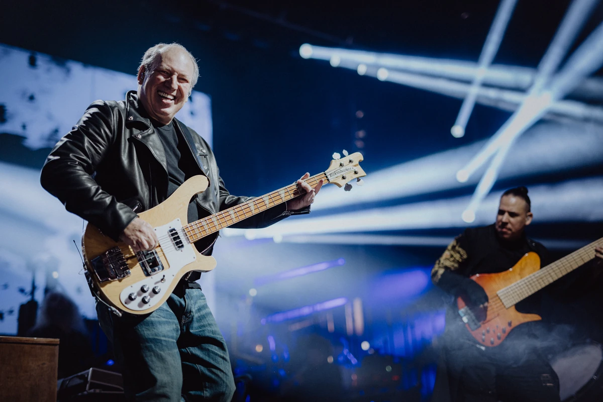 Hans Zimmer live auf der Bühne, voller Energie und mit seiner E-Gitarre in der Hand, begleitet von einem weiteren Musiker im Hintergrund. Die dynamische Beleuchtung verstärkt die kraftvolle Atmosphäre der Show.