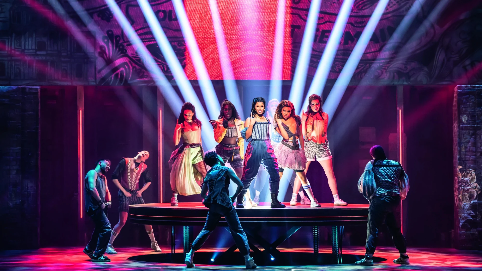 In einer lebhaften Bühnenshow zeigen Tänzerinnen und Tänzer in vielseitigen Outfits, mit farbenfroher Beleuchtung und dynamischen Posen Energie und Ausdruck.