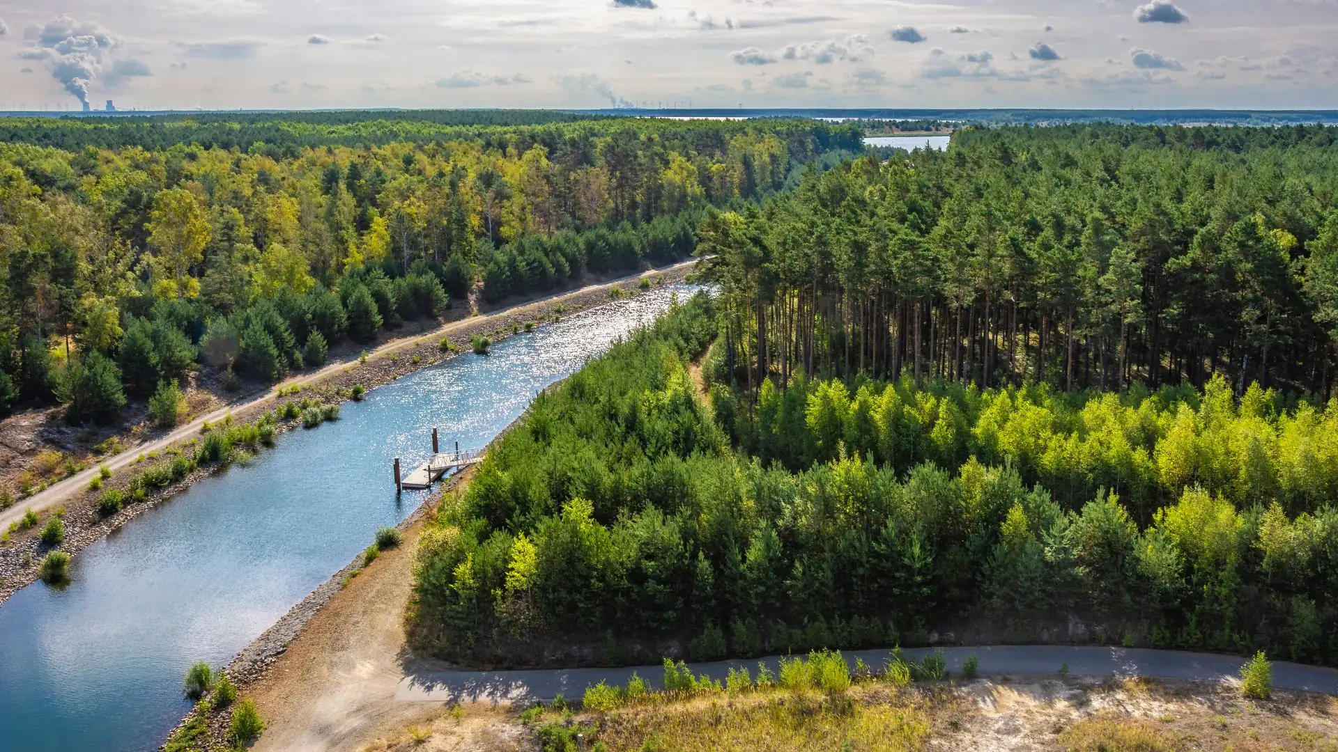 Luftaufnahme eines schmalen Kanals im Lausitzer Seenland, umgeben von dichtem Wald und einem kleinen Steg am Ufer