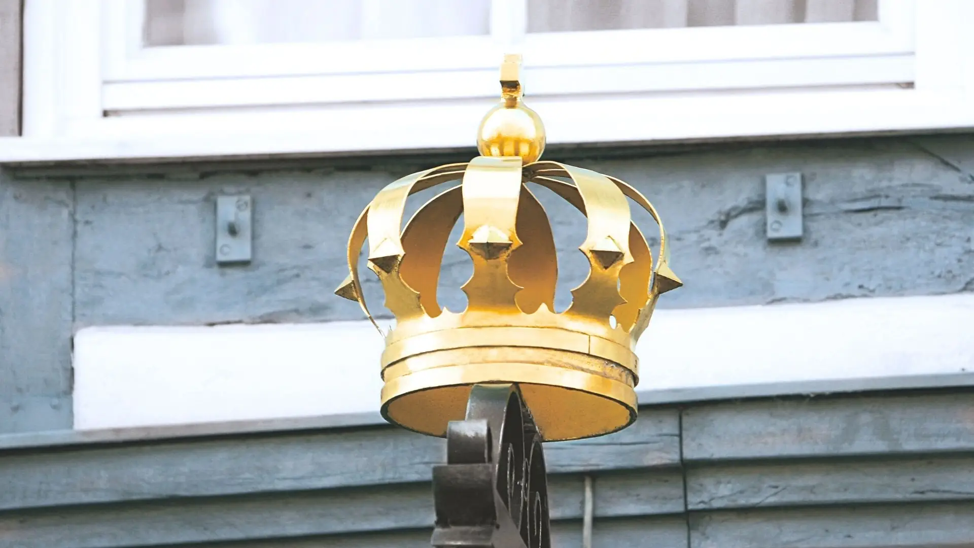 Goldene Krone auf schwarzem Metallpfosten vor dem Hotel mit Fenster