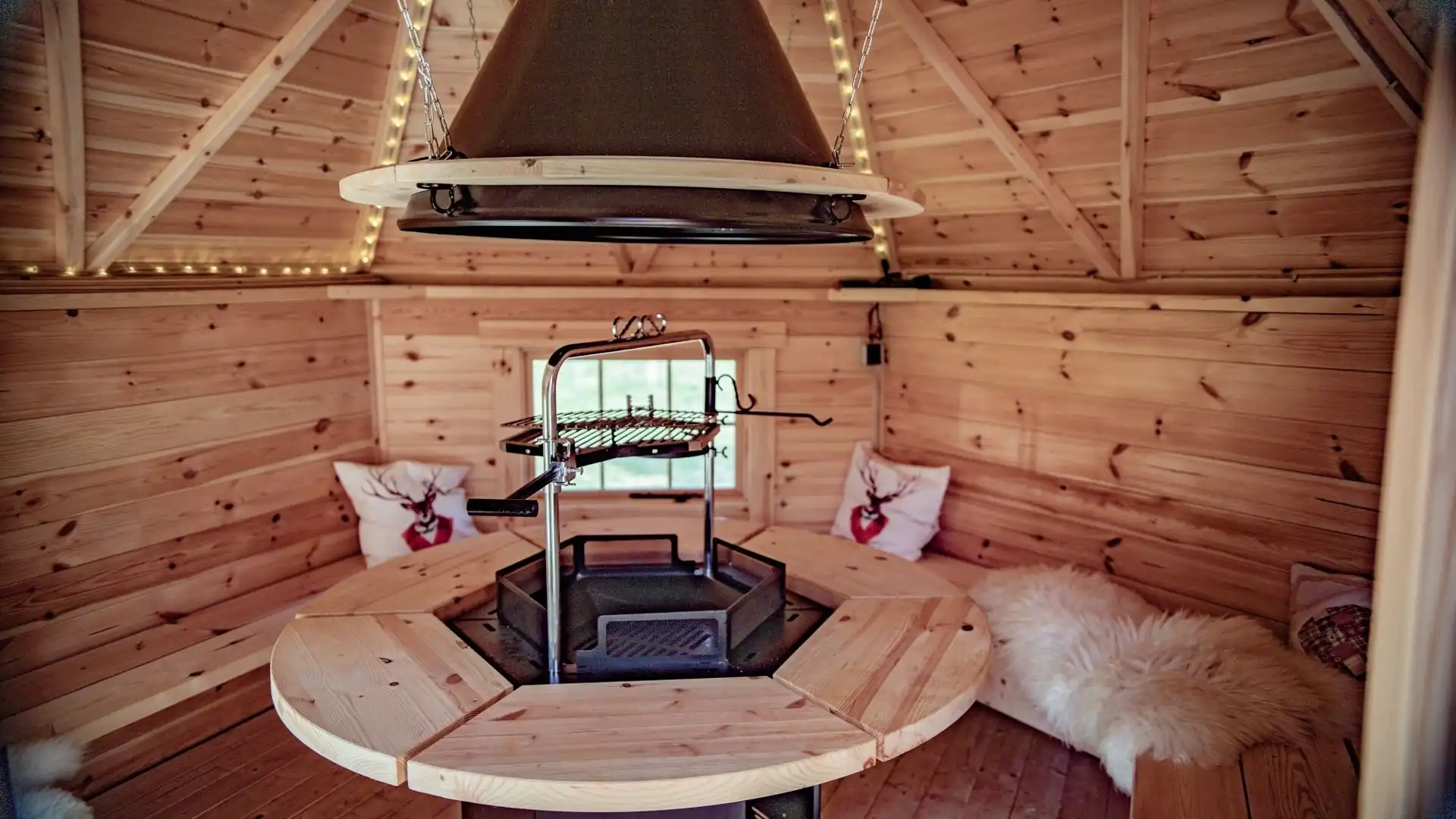 Runder Holztisch in einer hölzernen, runden Hütte mit Sitzkissen und Fellüberwurf auf der Bank