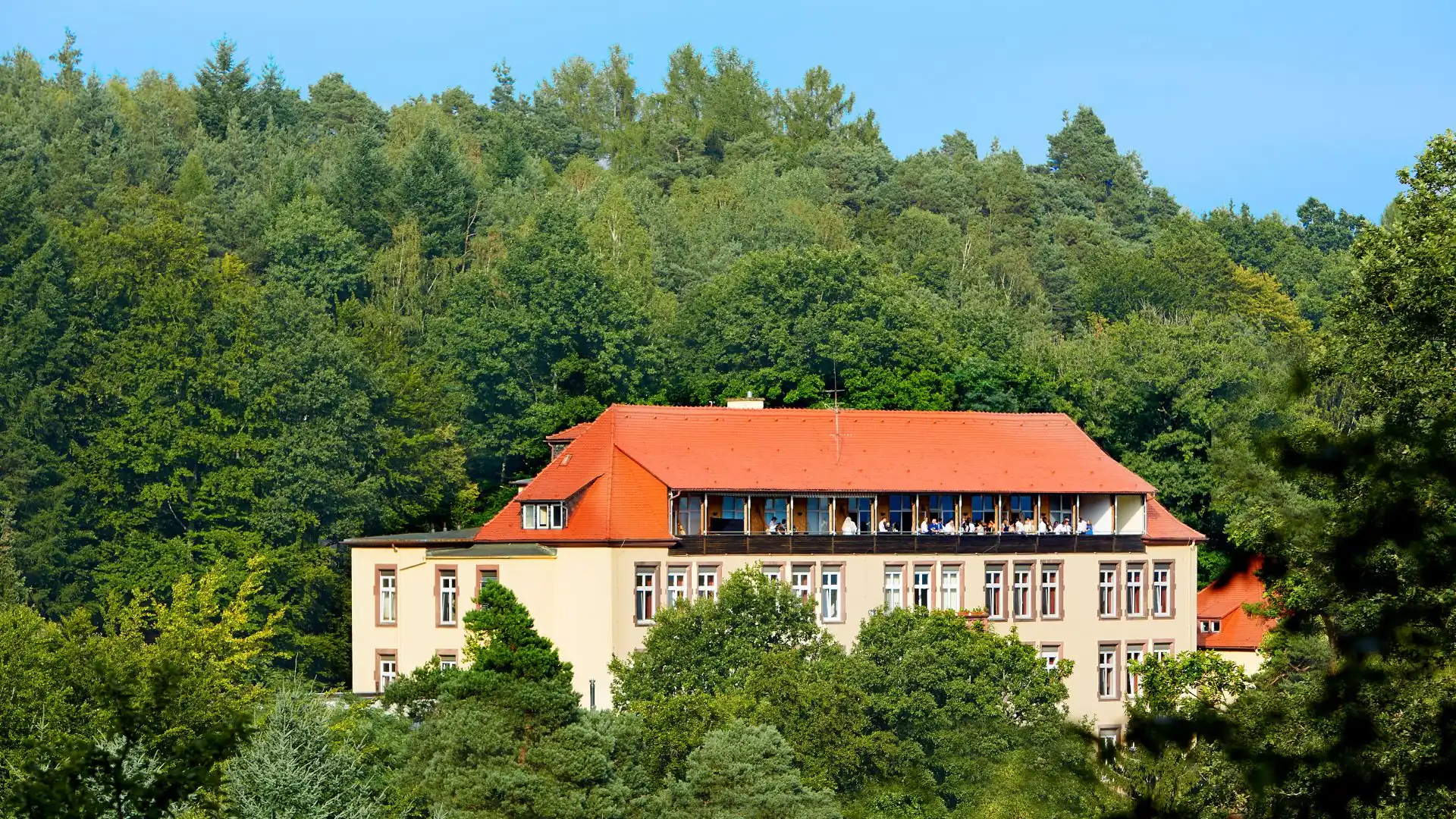HotelgebĂ€ude Franziskushöhe mit rotem Satteldach umgeben von dichtem Wald auf einem HĂŒgel