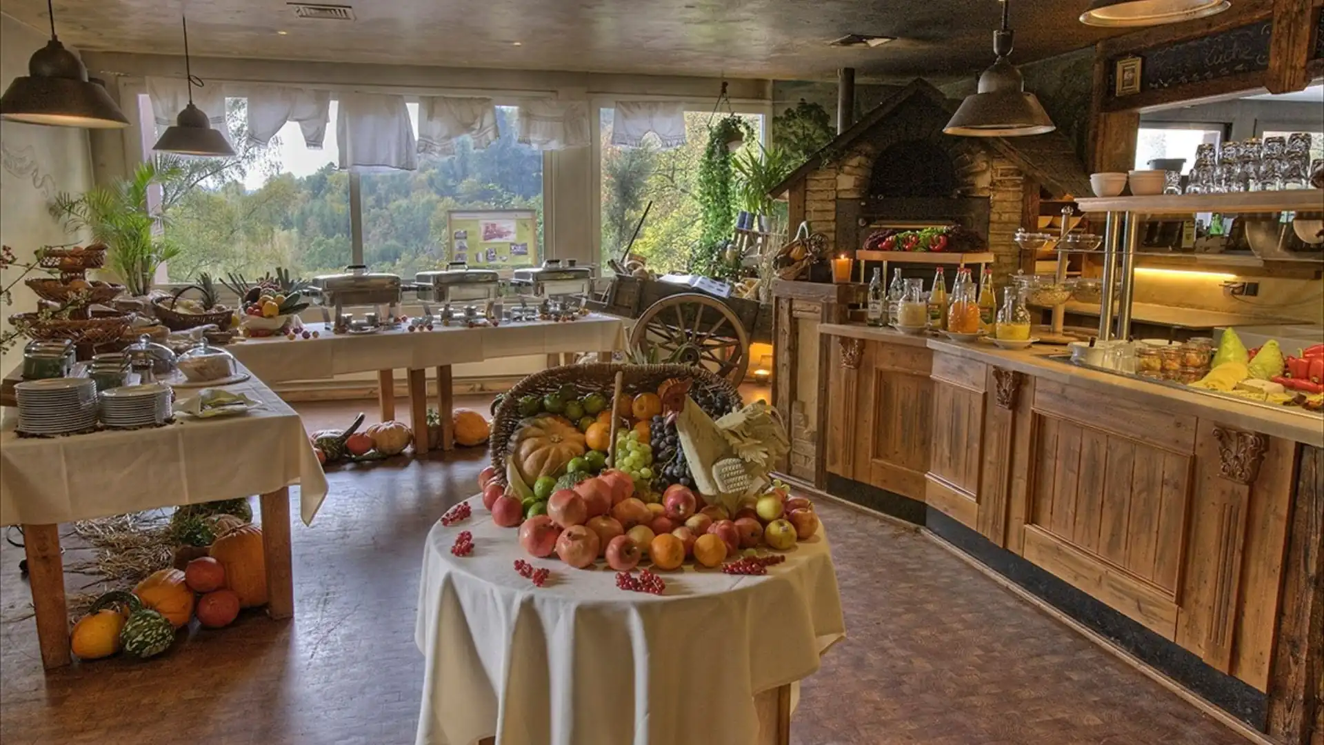 Buffet im Hotel Franziskushöhe mit rundem Tisch in der Mitte, darauf Obst und GemĂŒse, umgeben von Holzmöbeln und groĂen Fenstern mit Blick ins GrĂŒne