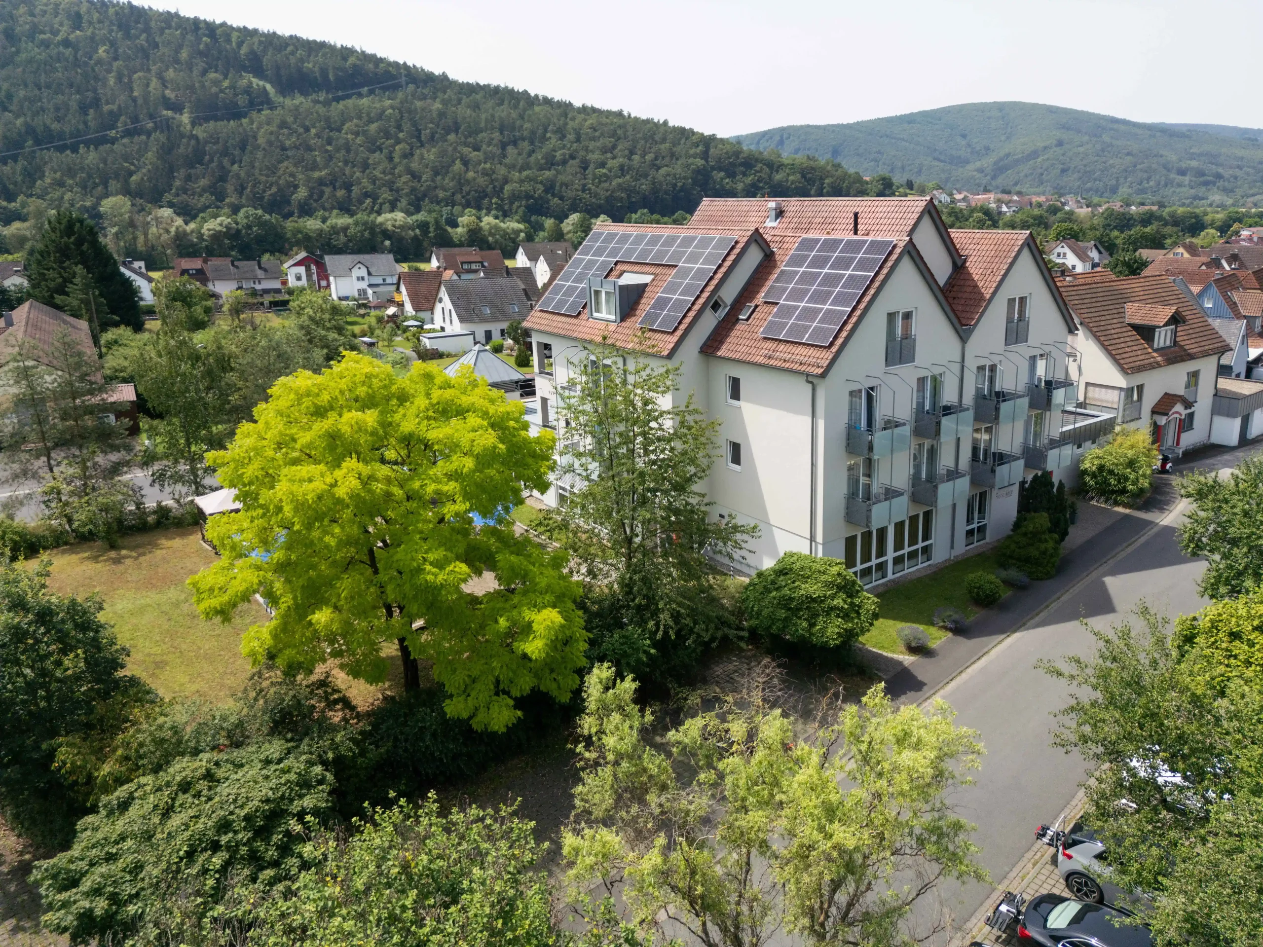 Luftaufnahme des Hotel Imhof mit Solarpaneelen auf dem Dach, umgeben von Bäumen und angrenzenden Wohnhäusern in einer grünen Hügellandschaft