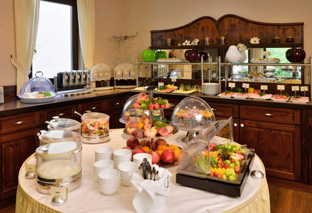 Buffet mit Obst, Aufschnitt, Müsli und Geschirr in einem Raum mit Holzschränken und Fenster