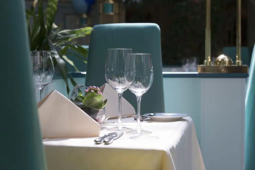 Gedeckter Tisch mit zwei Weingläsern, Besteck, Serviette und kleiner Pflanze in einem Restaurant