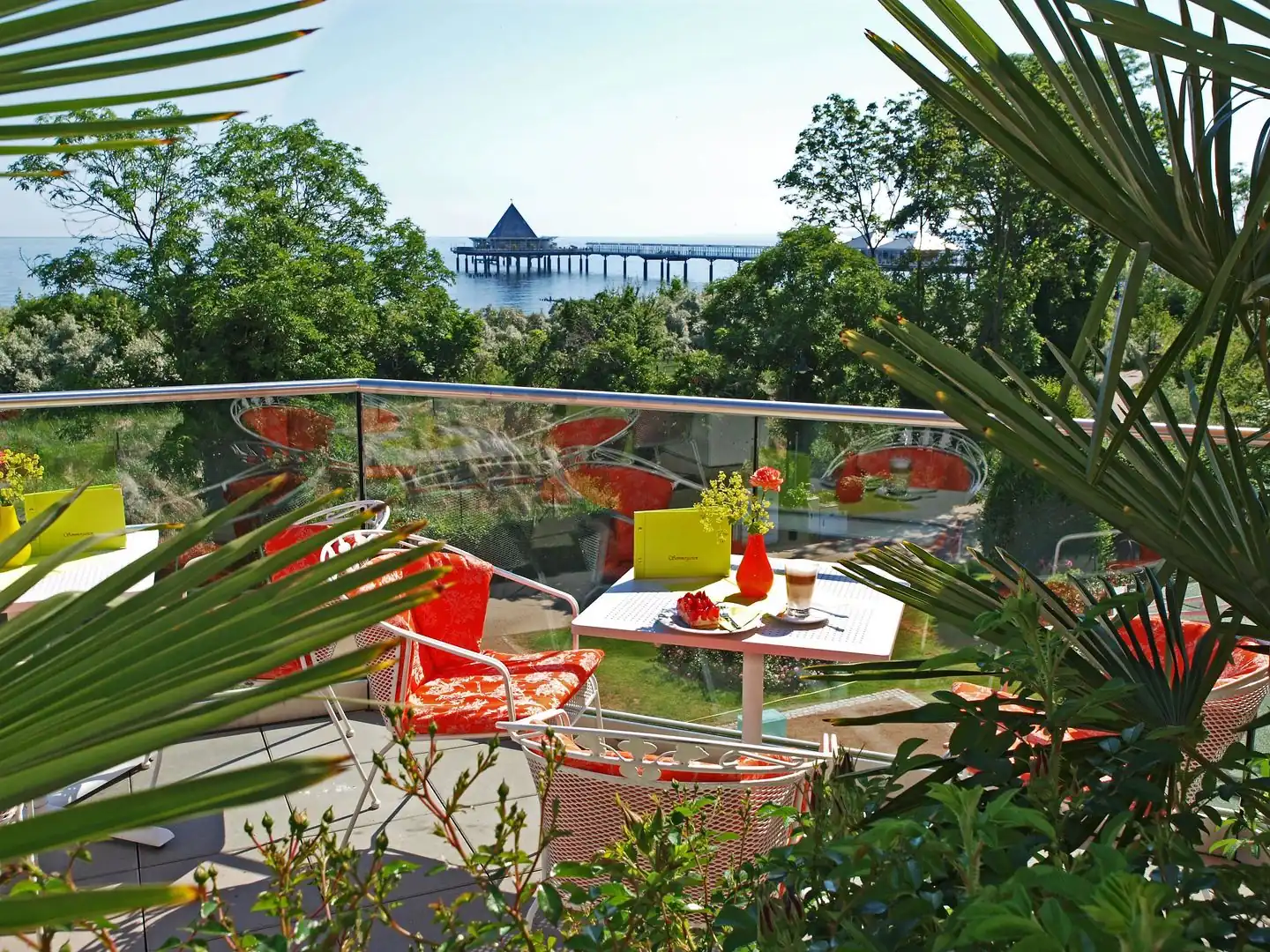 Terrasse mit Tisch, Stühlen und Pflanzen mit Blick auf eine Seebrücke über dem Meer