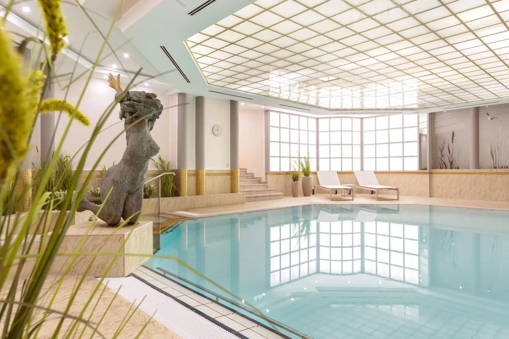 Innenansicht eines Wellnesspools mit einer Skulptur eines Pferdekopfes, großen Fenstern und Liegestühlen