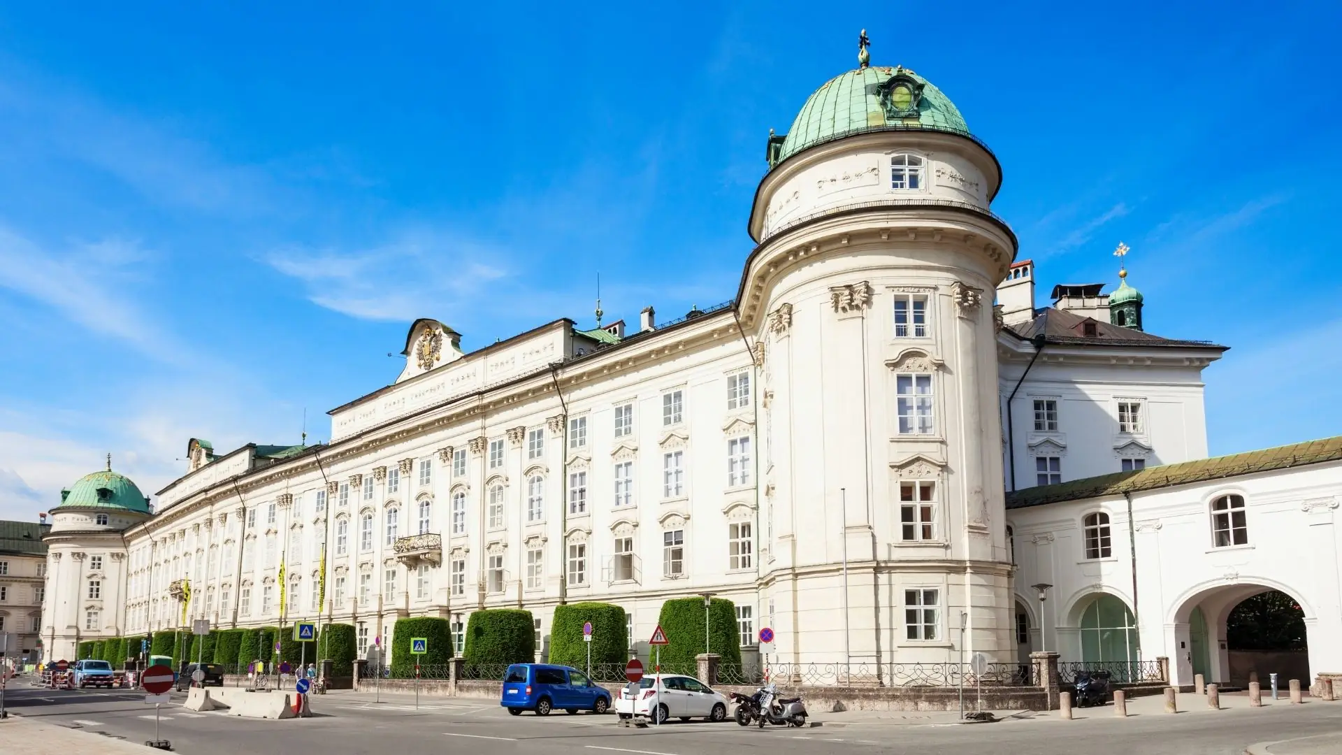 Weitläufiges barockes Gebäude der Kaiserlichen Hofburg Innsbruck mit mehreren Kuppeln und Arkadengang bei blauem Himmel