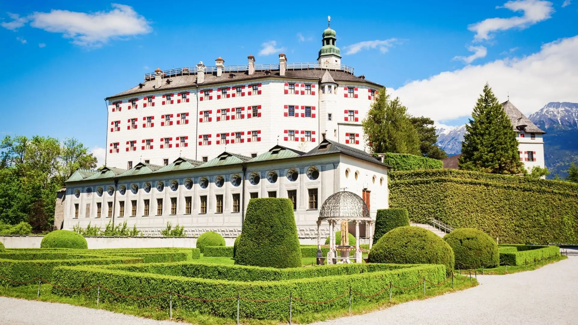 Schloss Ambras in Innsbruck mit gepflegtem Garten, symmetrischen Hecken und Bergen im Hintergrund