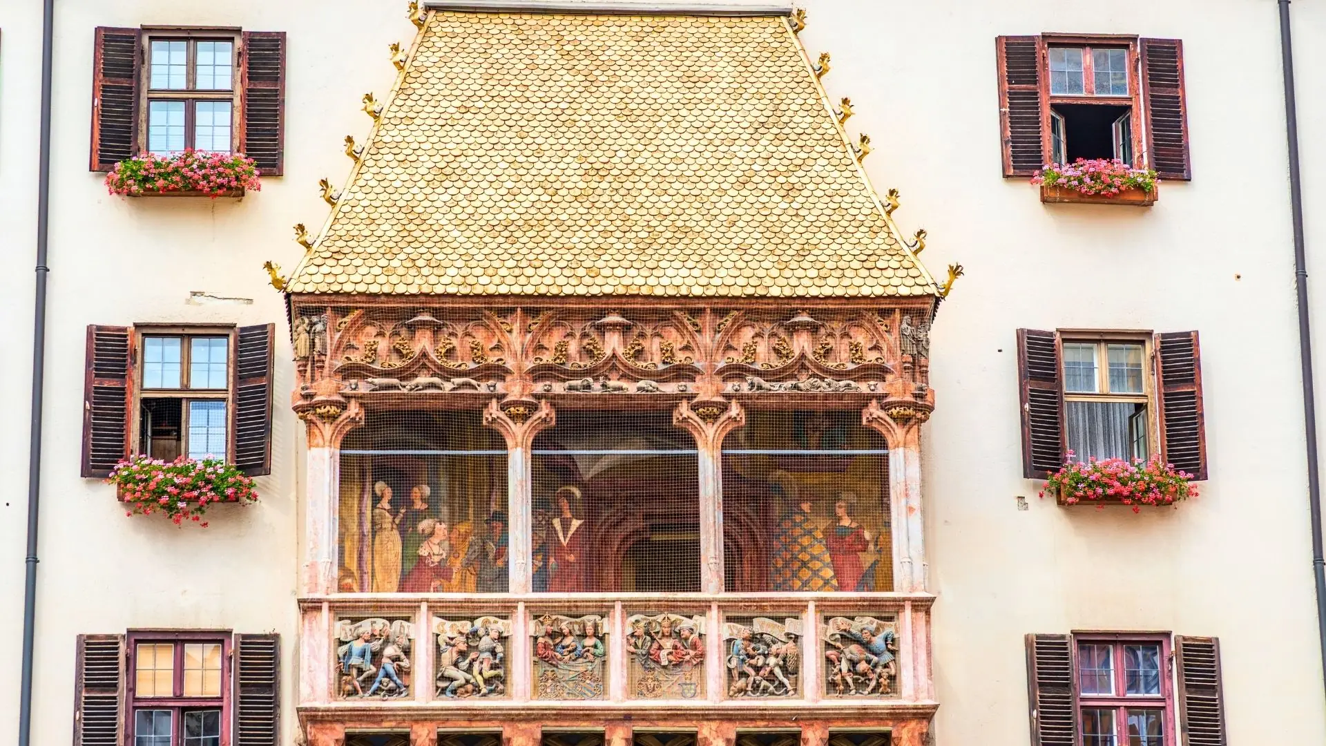 Das Goldene Dachl mit golden schimmerndem Dach und reich verzierten Arkaden an einem historischen Gebäude in Innsbruck umgeben von Fenstern mit roten Fensterläden und Blumenkästen