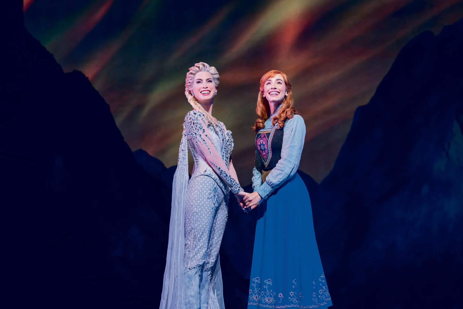 Disney Die EIskönigin Szenenbild; Anna und Elsa halten ihre Arme und schauen glücklich nach oben