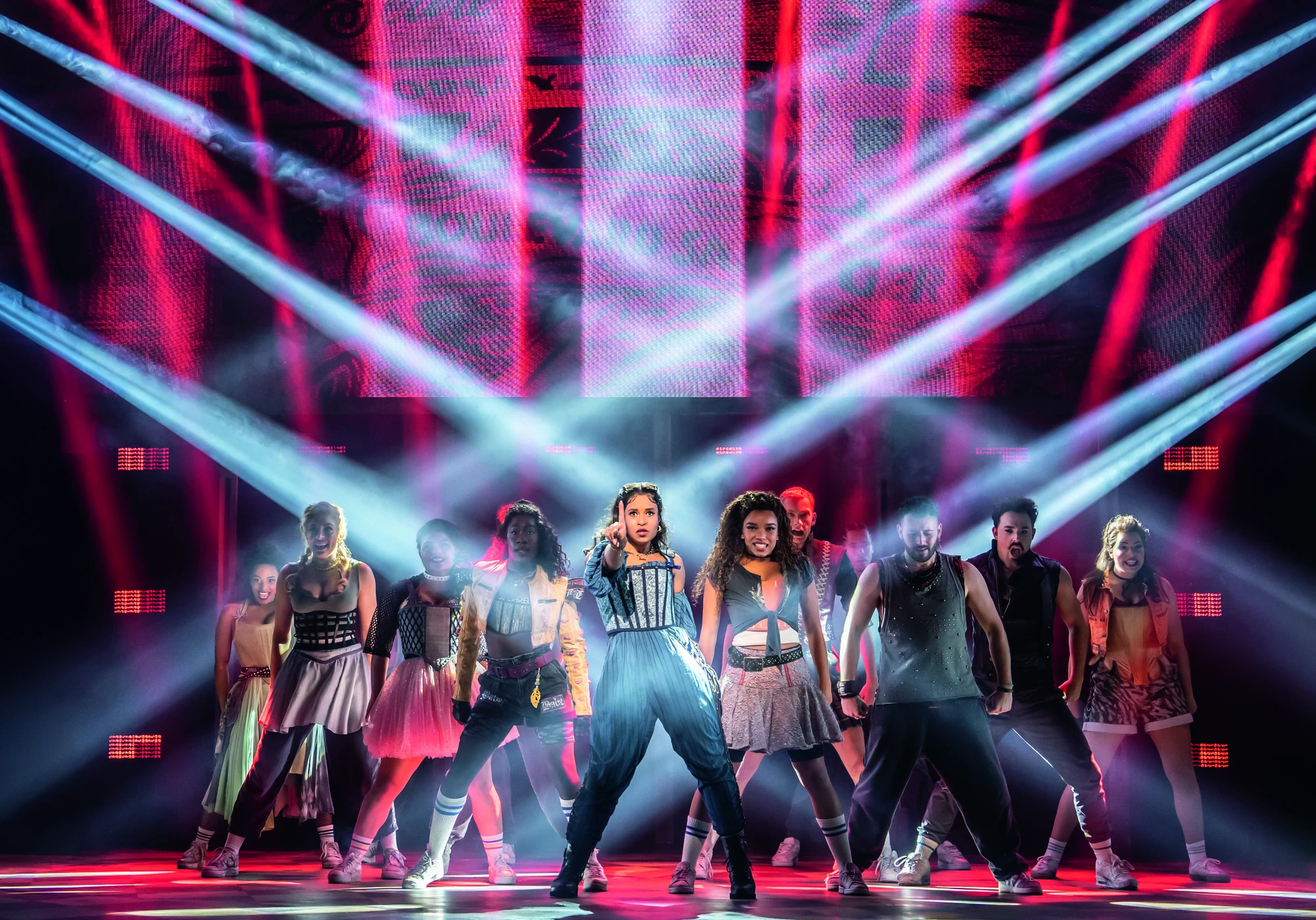 In einer lebhaften Bühnenshow zeigen Tänzerinnen und Tänzer in vielseitigen Outfits, mit farbenfroher Beleuchtung und dynamischen Posen Energie und Ausdruck.