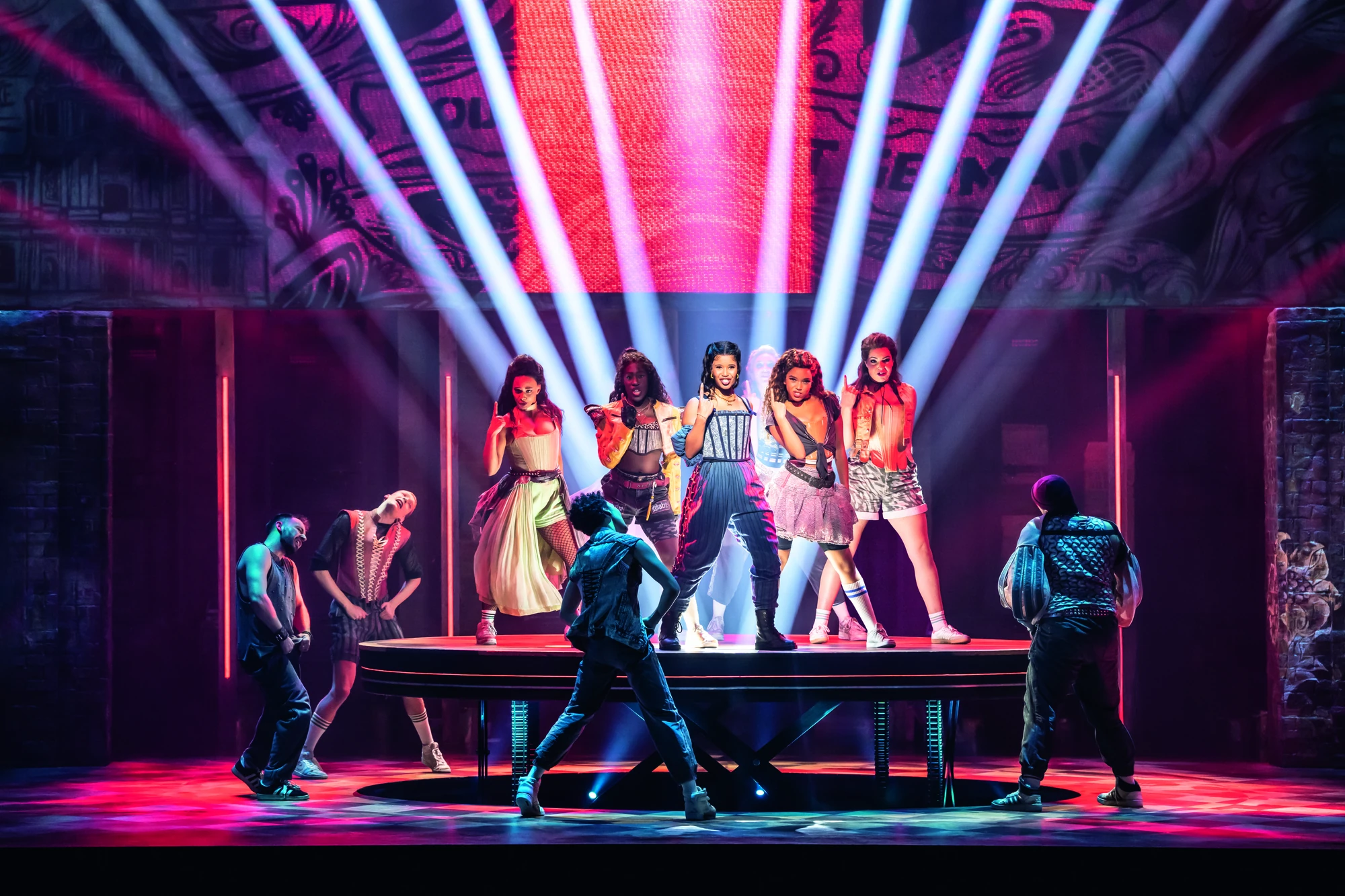 In einer lebhaften Bühnenshow zeigen Tänzerinnen und Tänzer in vielseitigen Outfits, mit farbenfroher Beleuchtung und dynamischen Posen Energie und Ausdruck.