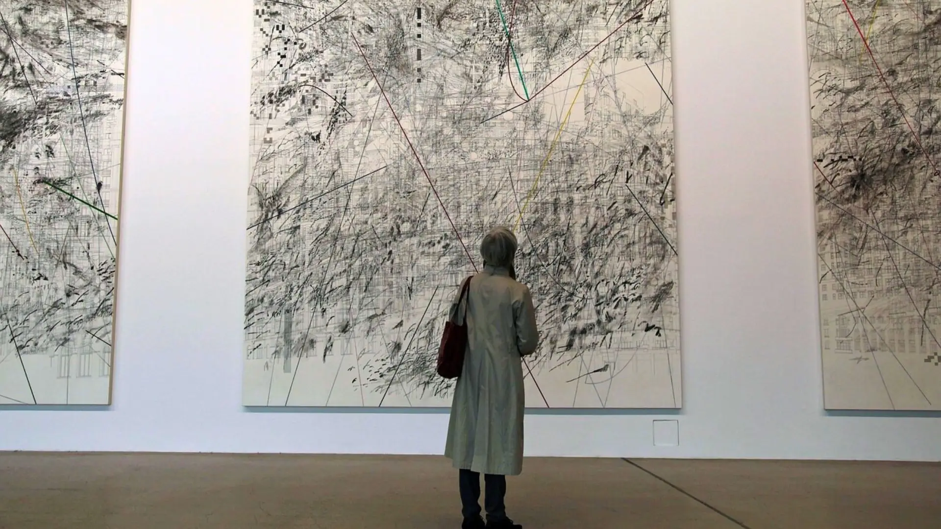 Person mit hellgrauem Mantel steht vor großem abstrakten Kunstwerk mit Linien und Punkten in Kassel.