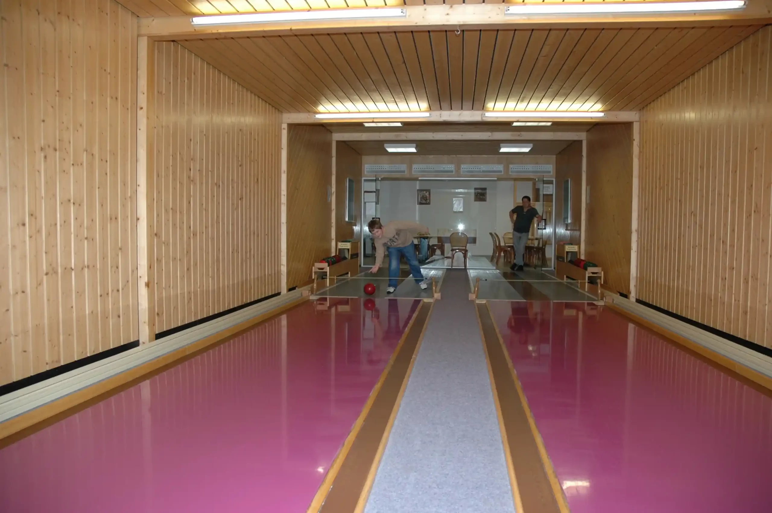 Zwei Personen spielen Kegeln in einer Kegelbahn mit Holzverkleidung und rosa Kegelbahnen im Hotel Imhof