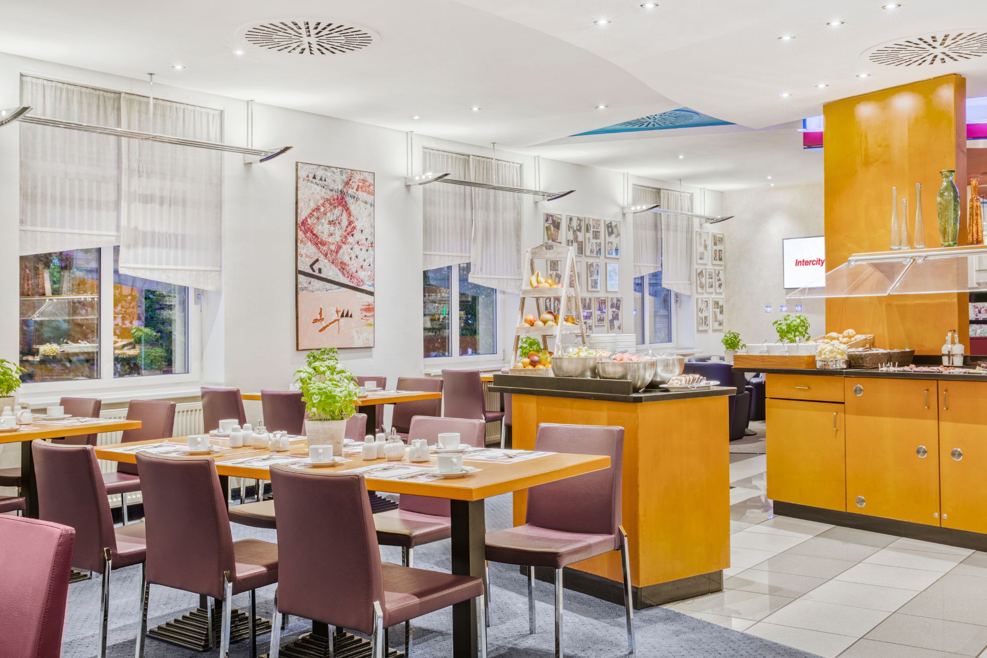 Ein moderner Essbereich mit ordentlich angeordneten Tischen, einer Buffetstation und Kunstwerken an den Wänden, die eine einladende Atmosphäre schaffen.