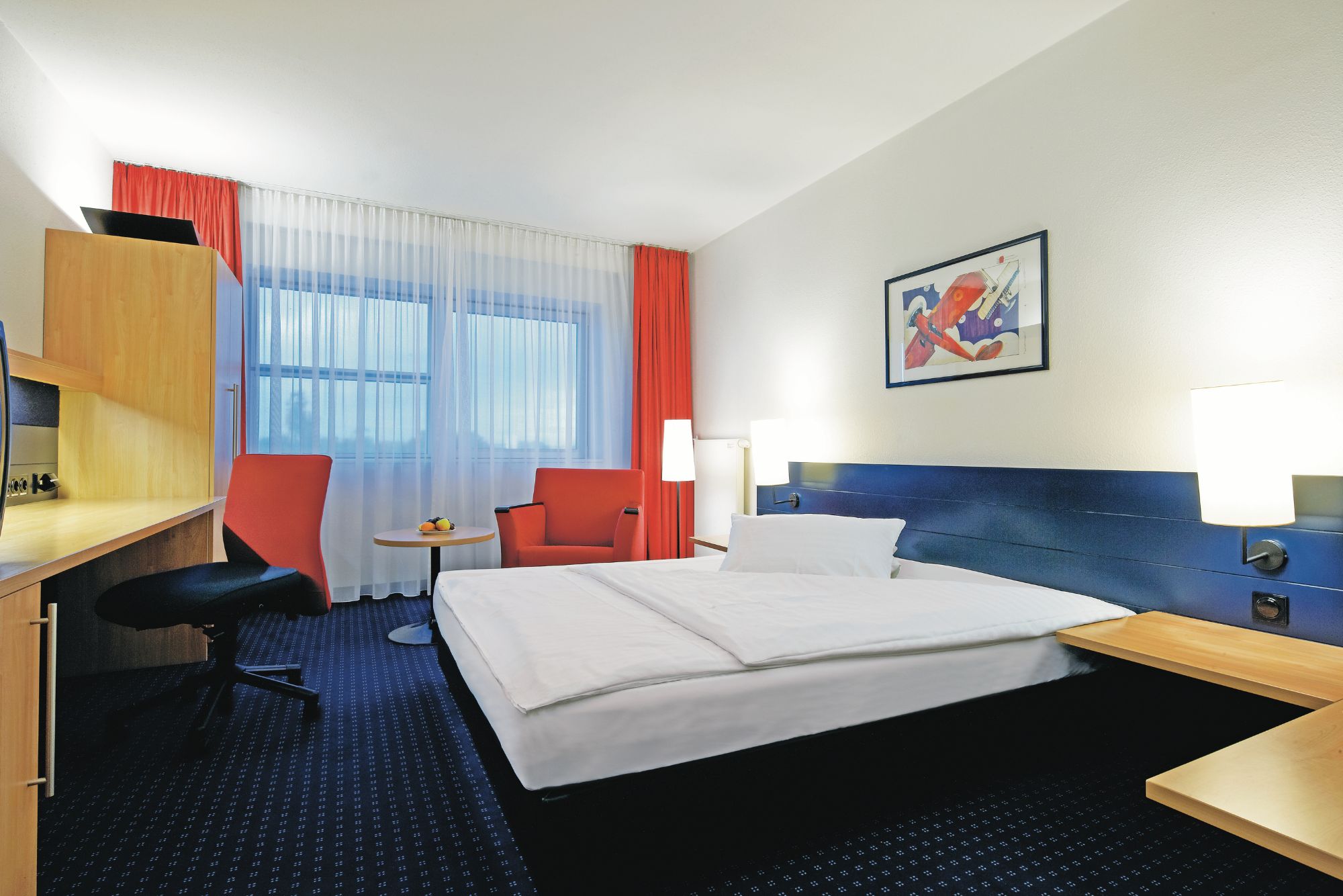 Ein gemütliches Hotelzimmer mit Doppelbett, Schreibtisch, roten Stühlen und hellen Vorhängen, moderner Einrichtung und sanfter Beleuchtung.