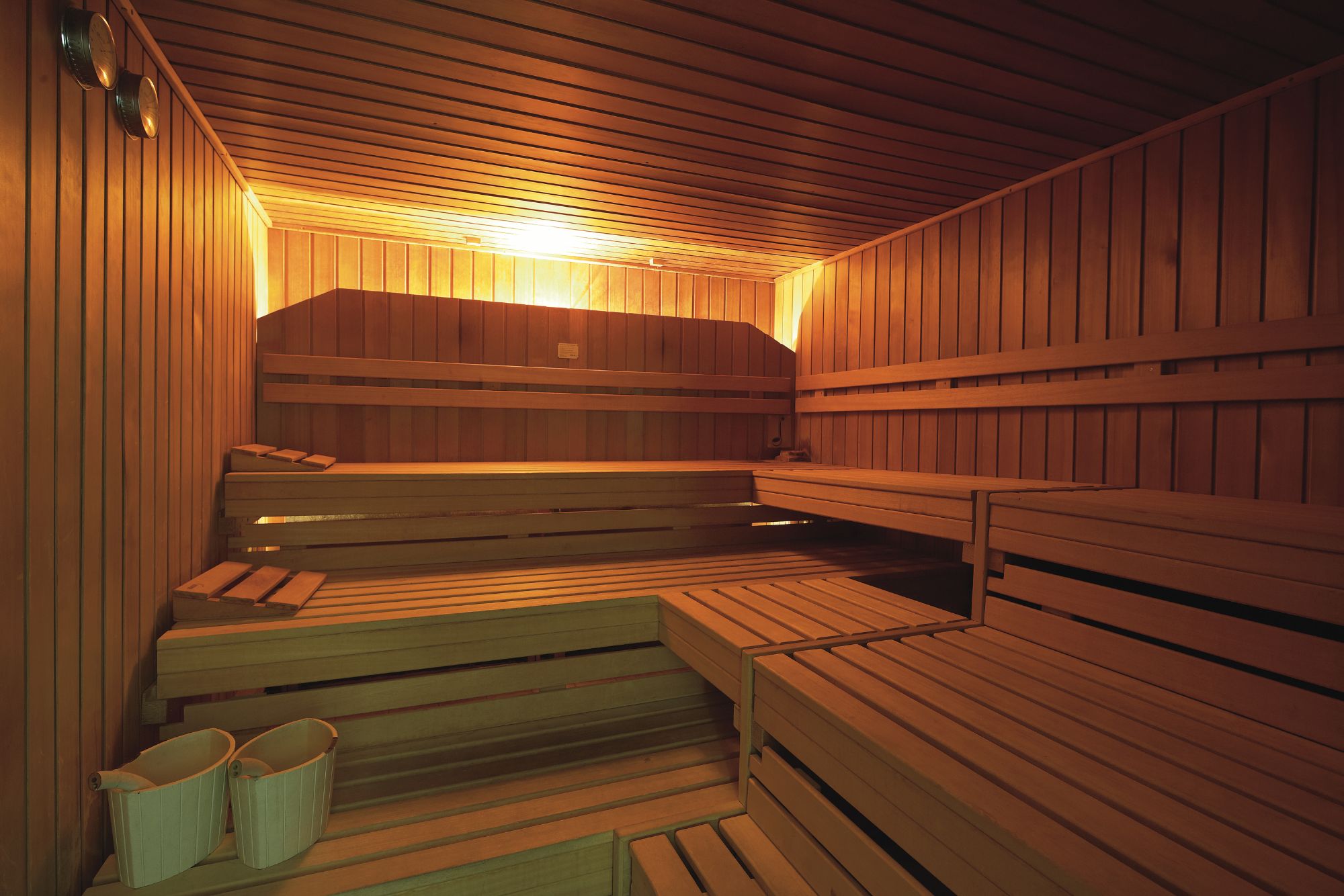 Innenraum einer Holzsauna mit Bänken, sanft beleuchtet durch warmes Umgebungslicht, das eine ruhige und entspannende Atmosphäre schafft.