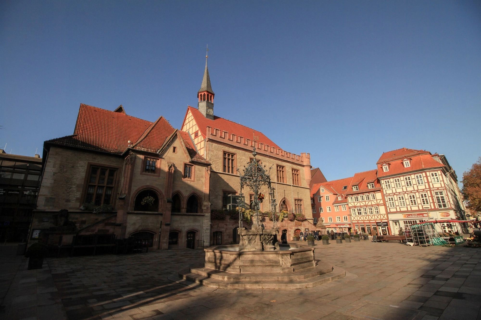 Historisches Rathaus mit Fachwerkhäusern und Brunnen auf gepflastertem Marktplatz unter blauem Himmel.