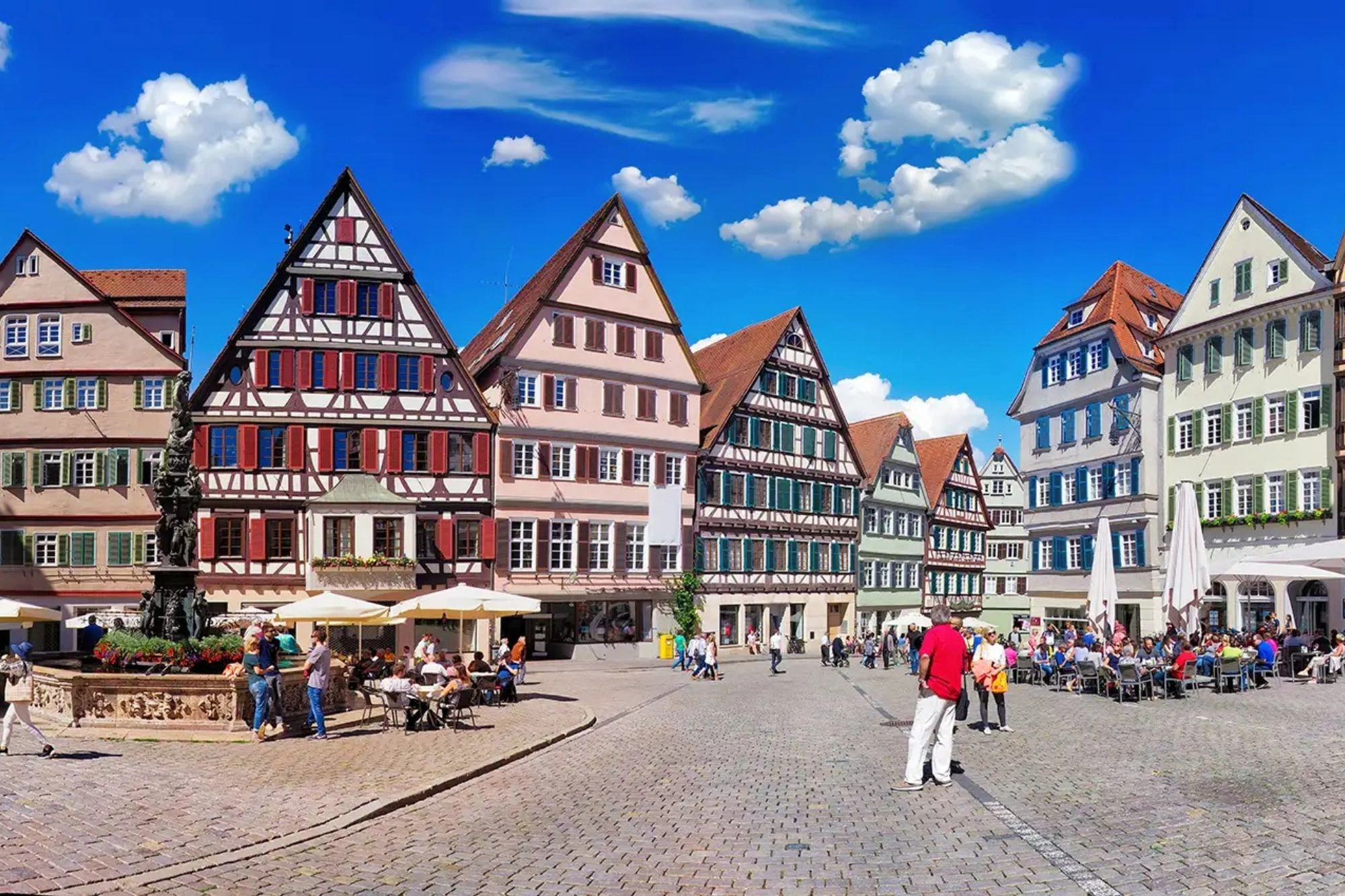 Panoramablick auf den Marktplatz mit Kopfsteinpflaster in Tübingen umrandet von bunten Fachwerkhäusern und vielen Spaziergängern