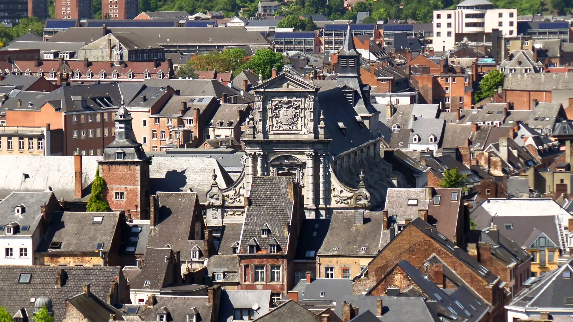 Dachlandschaft mit zahlreichen historischen Gebäuden und der Kirche Saint Loup in Namur, erkennbar an ihrem barocken Turm und der Fassade.