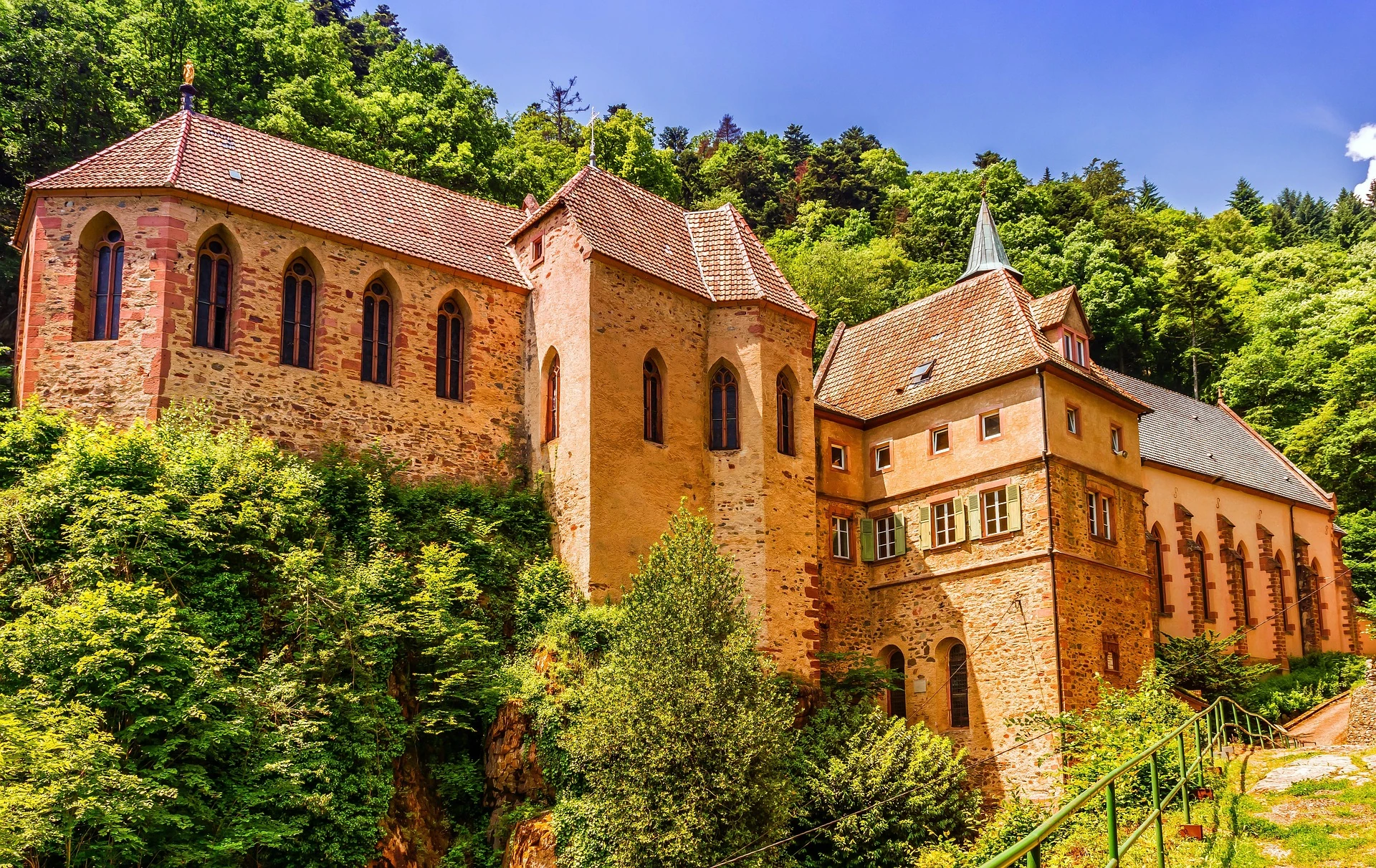 Historische Kirche im Elsass, erstrahlend im warmen Licht eines sonnigen Tages. Die Fassade zeigt kunstvolle Details und traditionelle Architektur, umgeben von einer malerischen Landschaft.