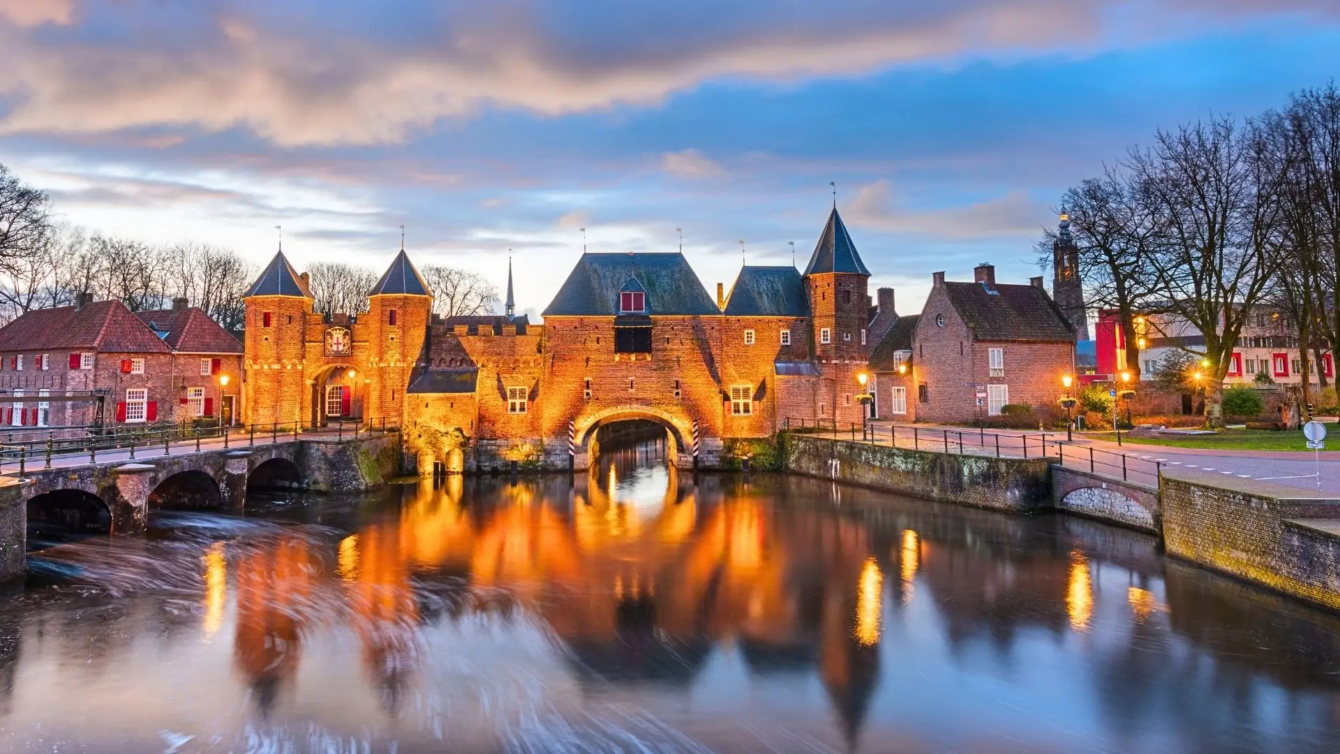 Illustration des beleuchteten Koppelpoort bei Abenddämmerung. Die historische Stadtmauer und der eindrucksvolle Torturm erstrahlen im warmen Licht, während der Himmel in sanften Dämmerungstönen leuchtet und eine malerische Atmosphäre schafft.