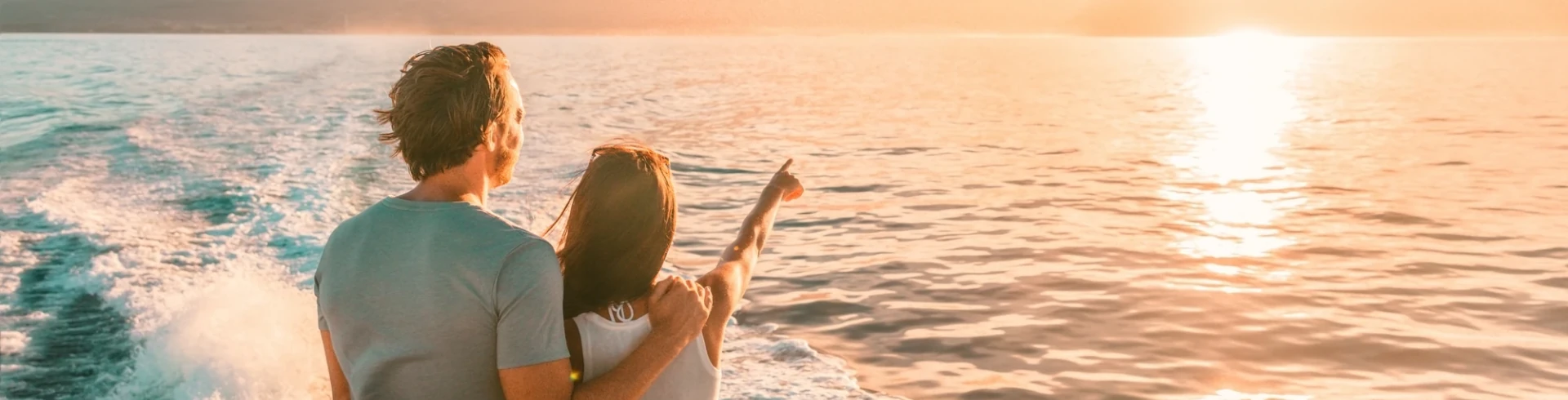 Paar auf einem Boot schaut auf den Sonnenuntergang über dem ruhigen Meer