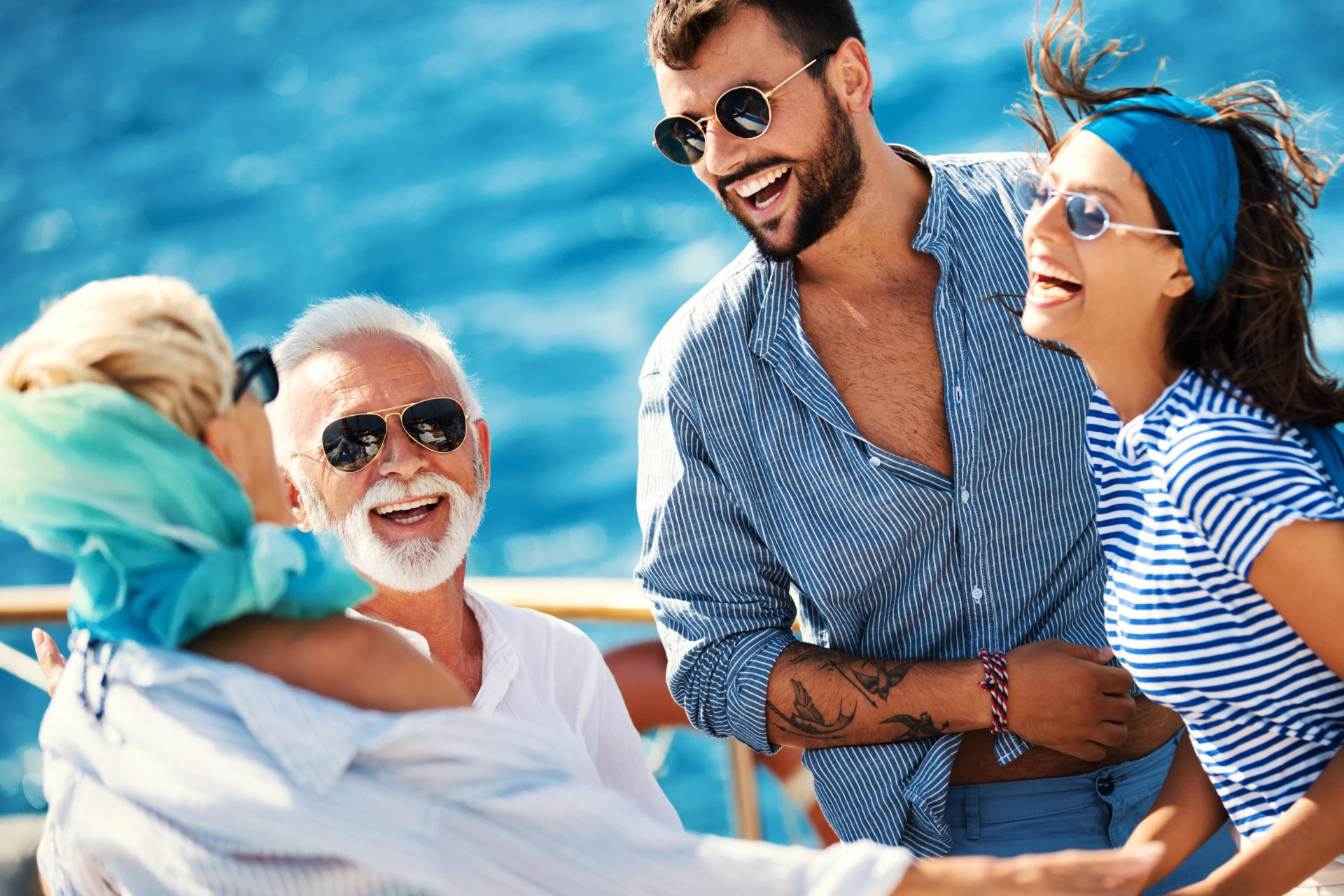Vier fröhliche Menschen unterschiedlichen Alters lachen zusammen auf einem Boot bei sonnigem Wetter am Meer