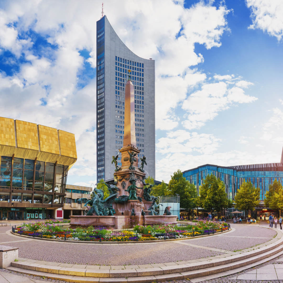 Dieses Foto zeigt den Augustusplatz in Leipzig mit dem Mendebrunnen im Vordergrund. Dahinter ragt das markante City-Hochhaus empor, flankiert von der modernen Universitätsbibliothek und dem Opernhaus, die das Stadtbild mit einer Mischung aus historischer und zeitgenössischer Architektur prägen.