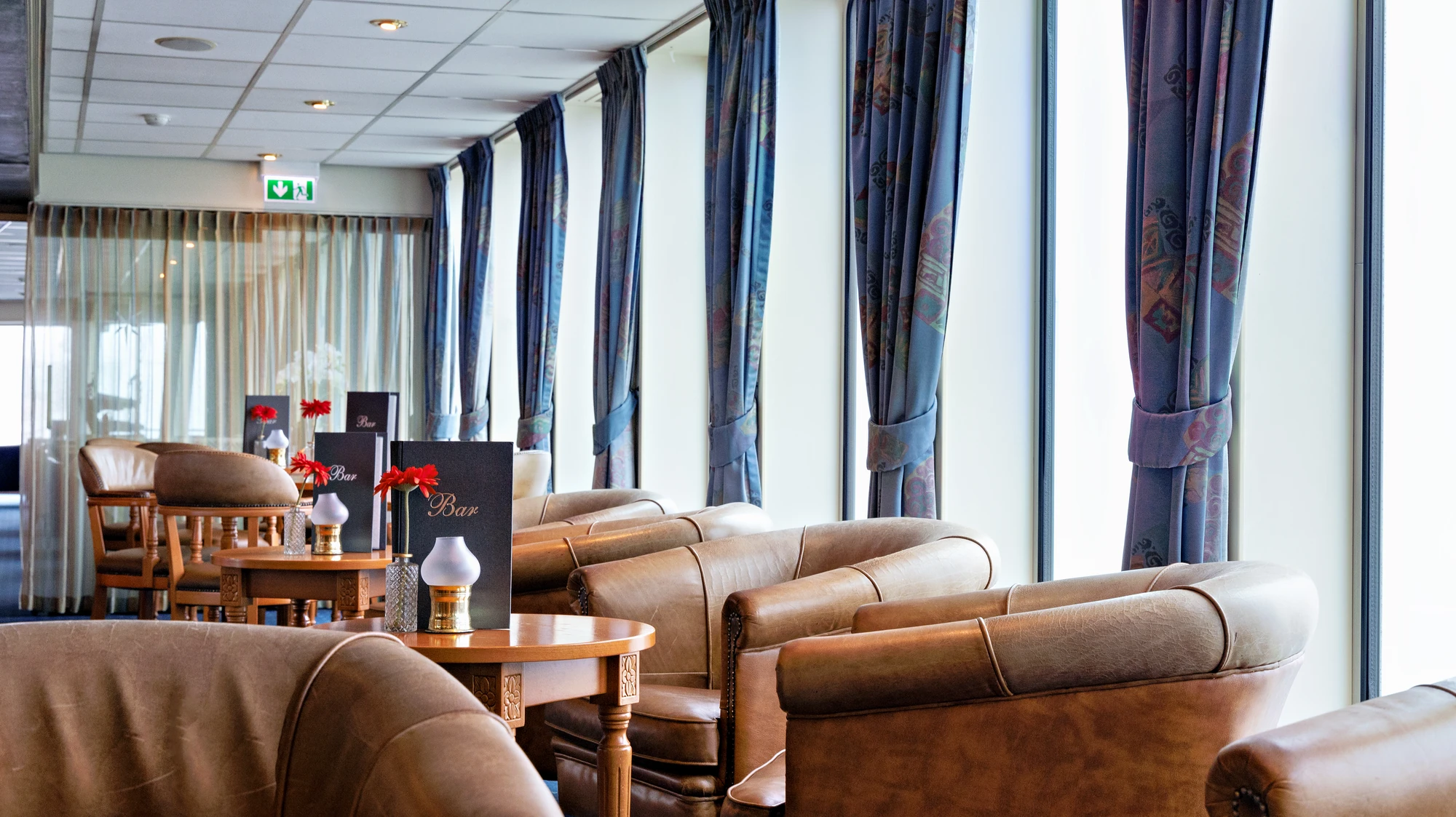 Sonnendach mit mehreren Tischen und Klappstühlen auf dem Holzdeck eines Flusskreuzfahrtschiffs, links und rechts grüne Liegestühle.