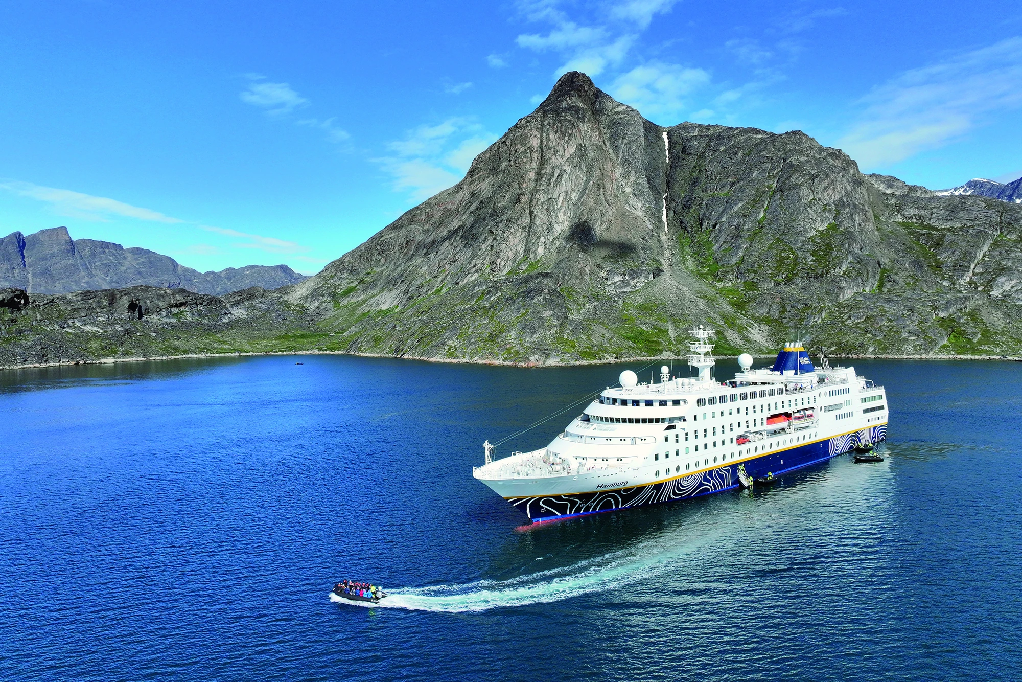 Ein Schiff auf dem blauen Wasser, umgeben von majestätischen Bergen.