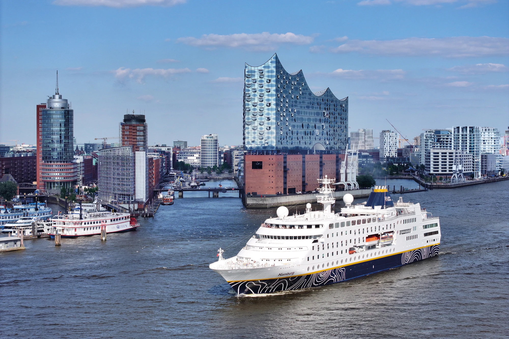 Kreuzfahrtschiff auf dem Hamburger Hafen mit moderner Architektur im Hintergrund.