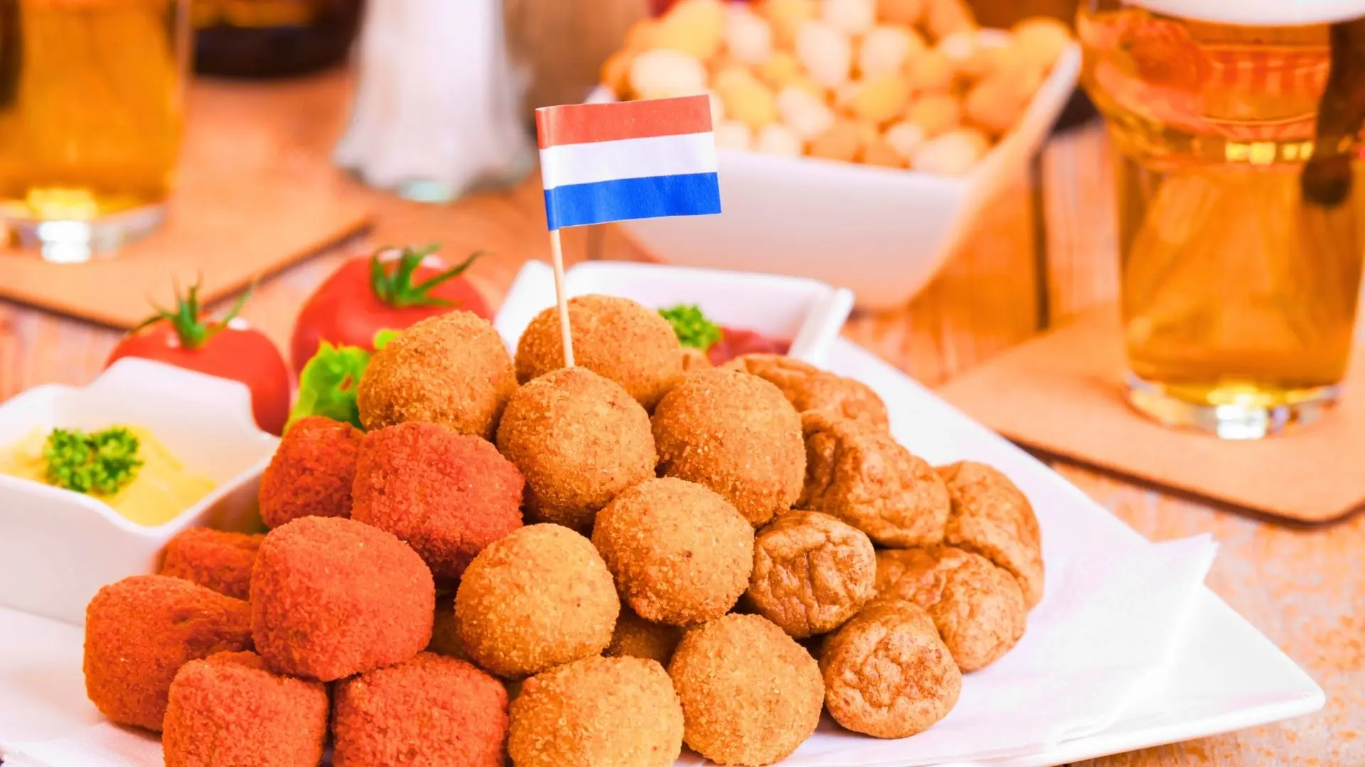 Verschiedene Sorten Bitterballen auf weißem Teller, garniert mit Tomaten, grüner Petersilie und niederländischer Flagge.