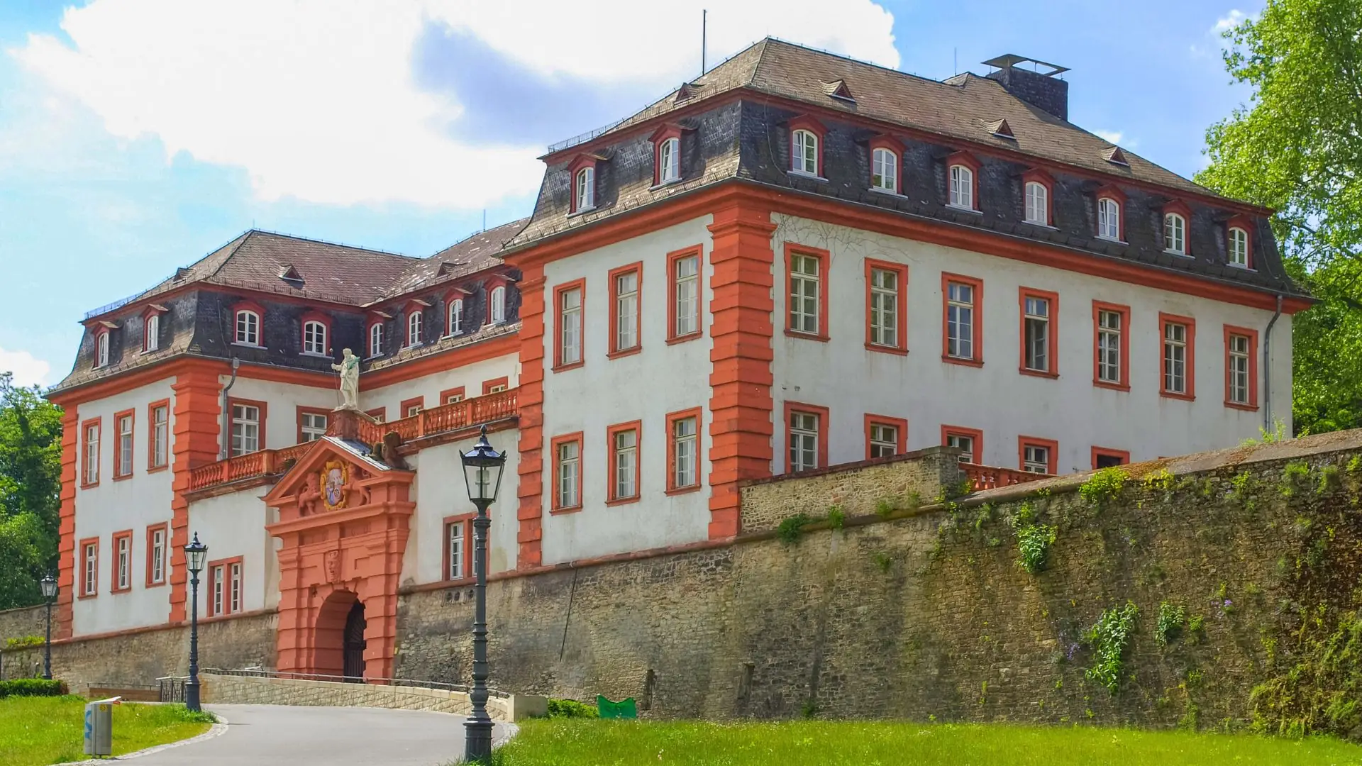 Historisches Gebäude der Zitadelle Mainz mit roten Fensterrahmen und einem Torbogen, umgeben von einer Steinmauer und Bäumen im Hintergrund
