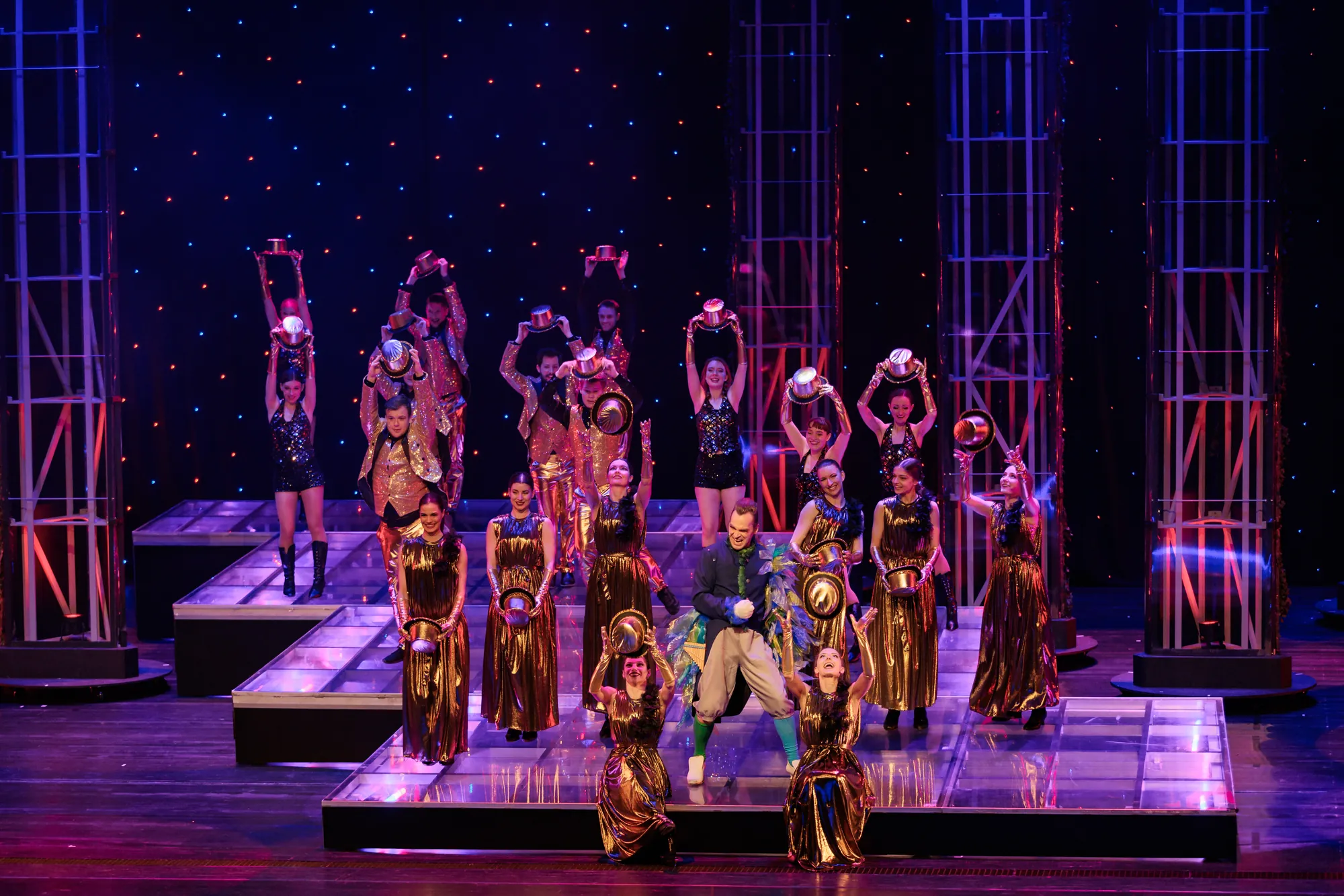 Ensemble aus Tänzerinnen in goldenen Kleidern, in der Mitte Papageno