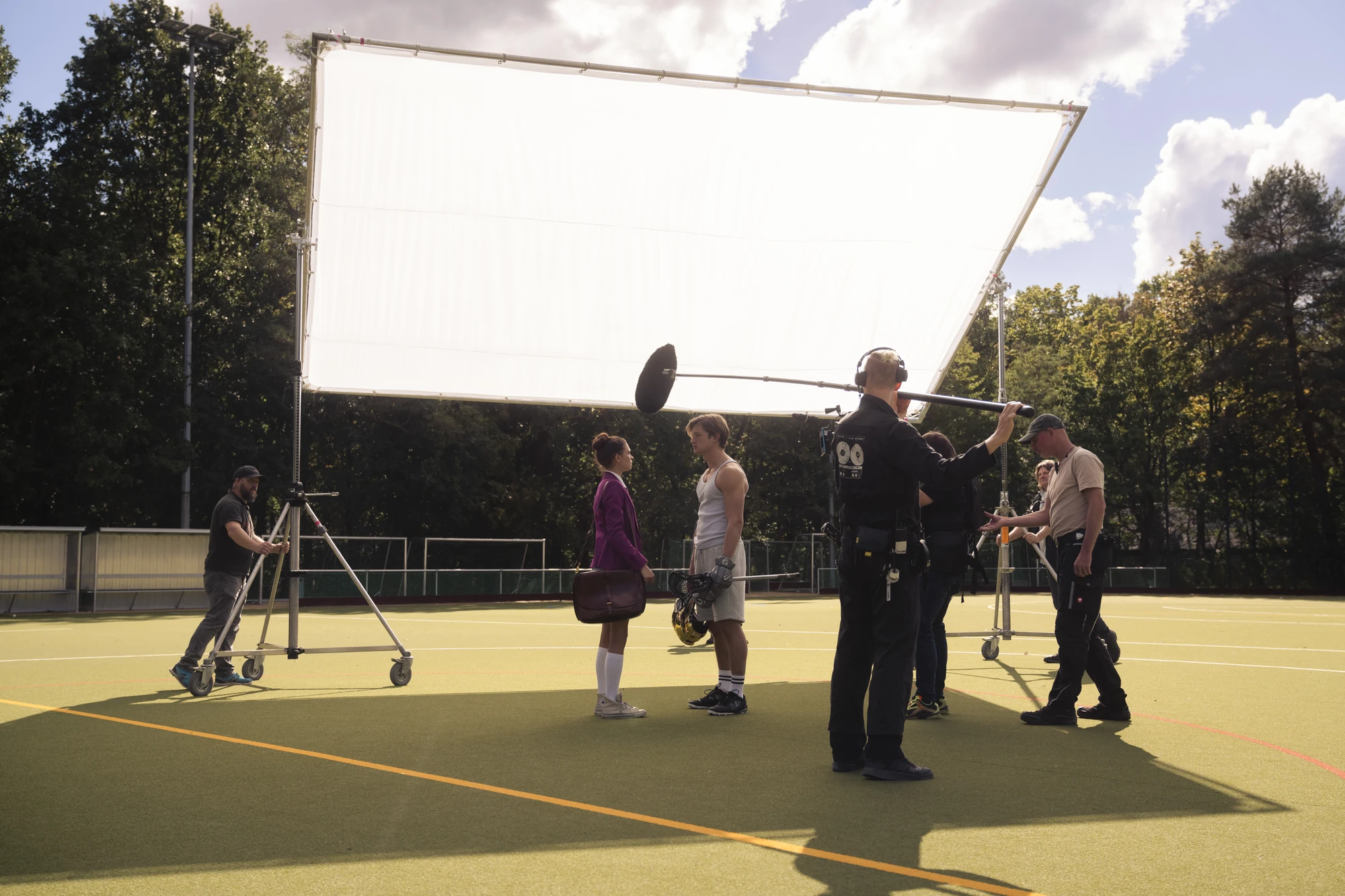 Blick hinter die Kulissen: Dreharbeiten auf dem Sportplatz von Maxton Hall. Die Crew bereitet eine Szene zwischen Lydia und James vor, im Fokus stehen große Licht- und Tonausrüstung