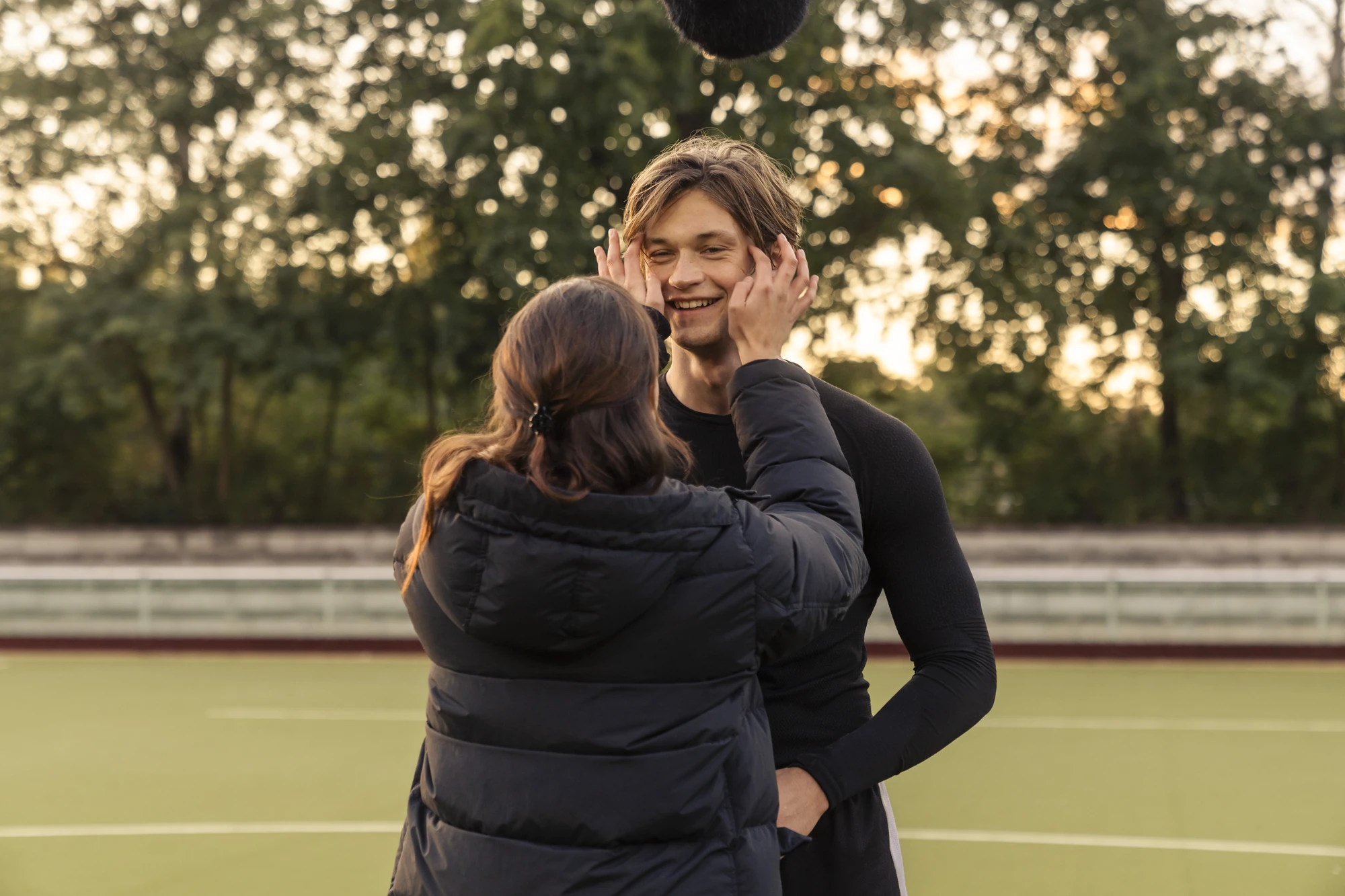 Maxton Hall Dreharbeiten zeigt einen herzlichen Moment zwischen Ruby und James auf dem Sportplatz, wo Ruby den lächelnden James am Gesicht in ihren Händen hält.