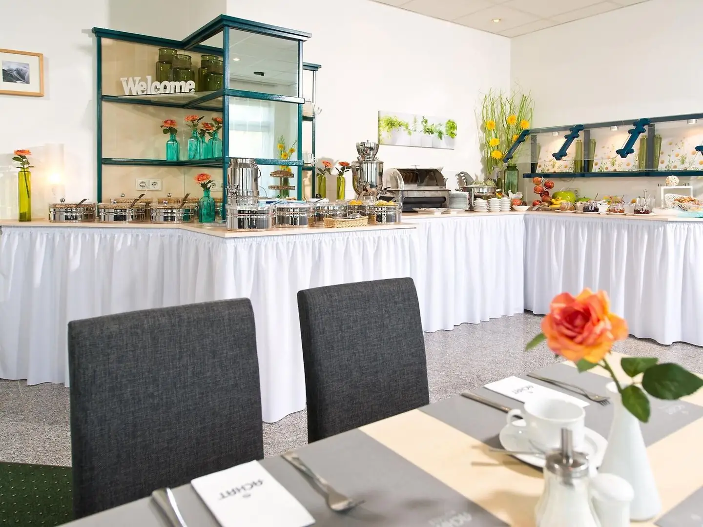 Buffet mit gedecktem Tisch und orangefarbener Blume im ACHAT Hotel Monheim am Rhein