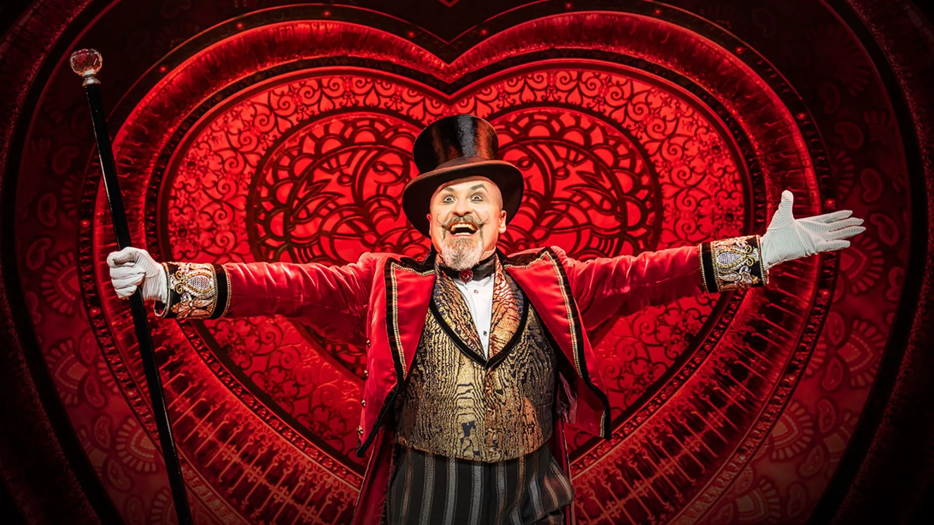 Eine künstlerische Bühnenkulisse mit einem Darsteller, der einen Spazierstock hält und die Arme weit ausbreitet.