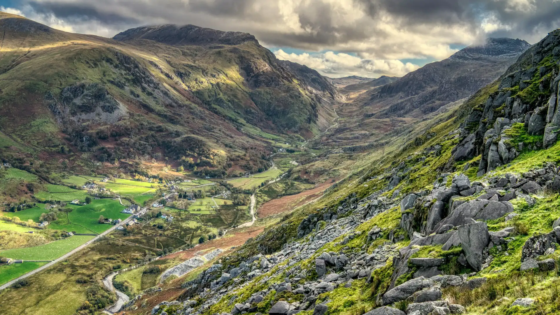 Bergtal im Schatten des Mount Snowdon mit grünen Wiesen, felsigen Hängen und bewölktem Himmel