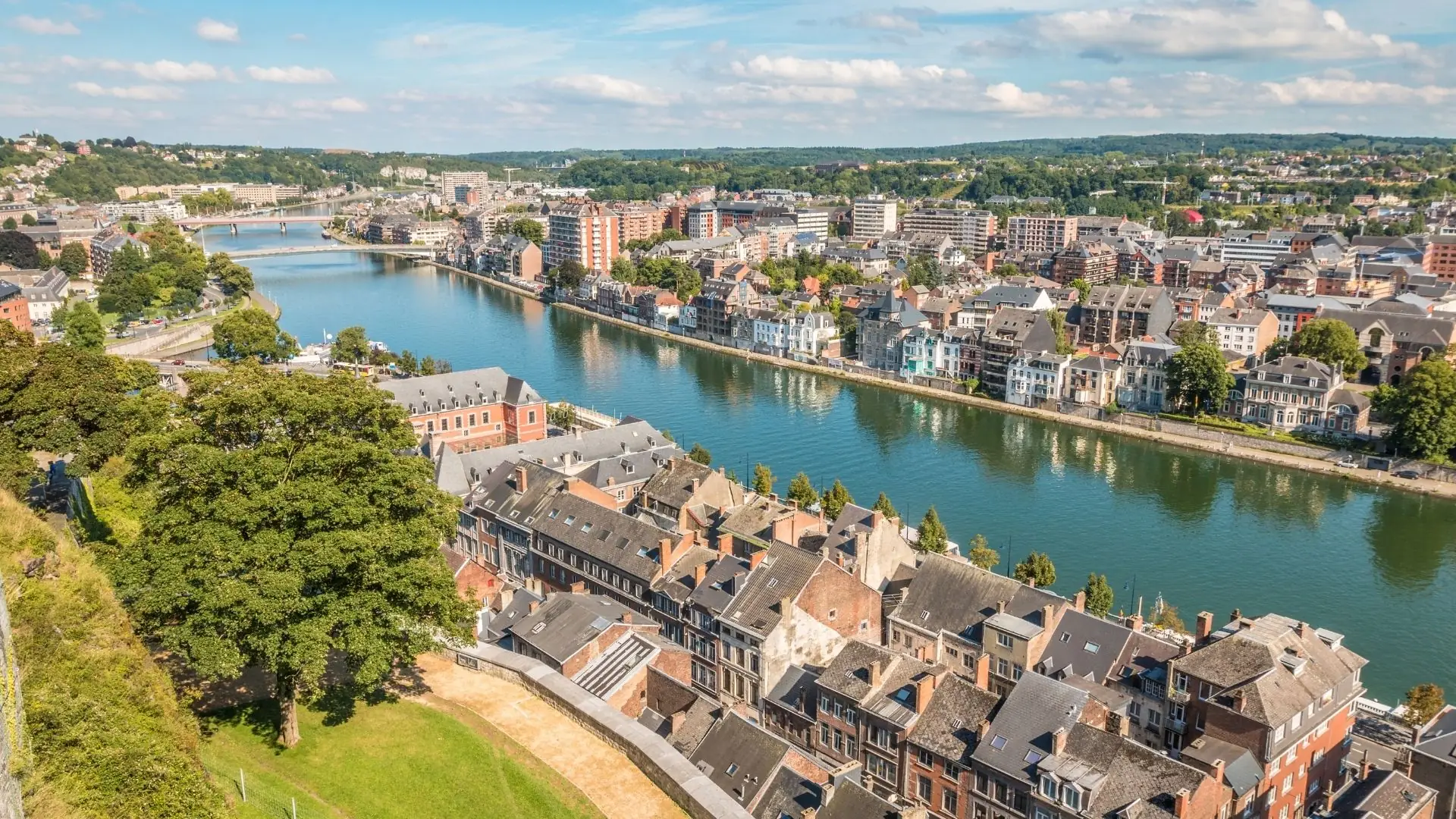 Luftaufnahme der Stadt Namur mit Fluss, Brücken und dicht bebauten Häusern unter blauem Himmel mit Wolken