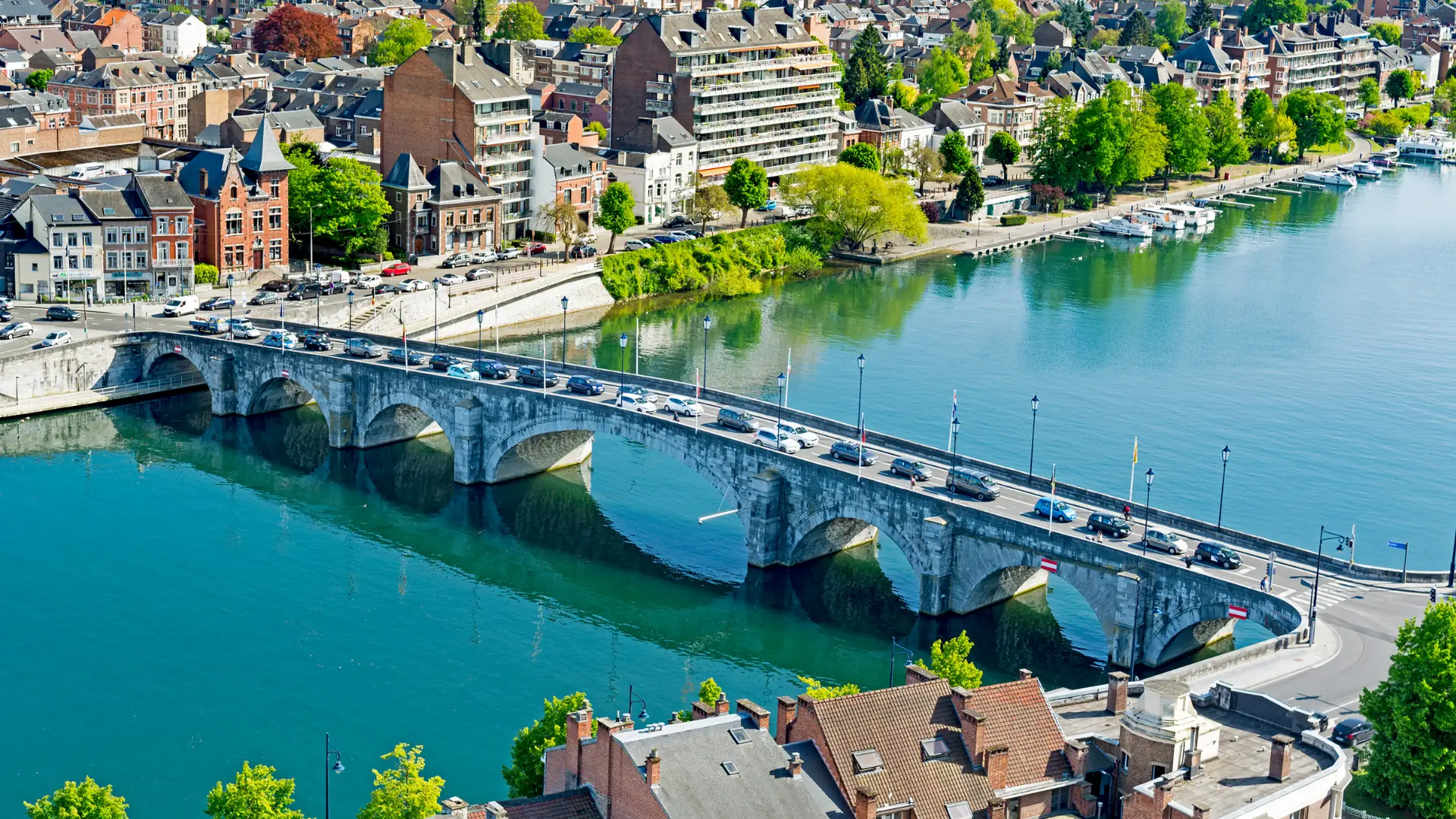 Luftaufnahme einer steinernen Bogenbrücke über einen Fluss mit Fahrzeugen und Häusern am Ufer