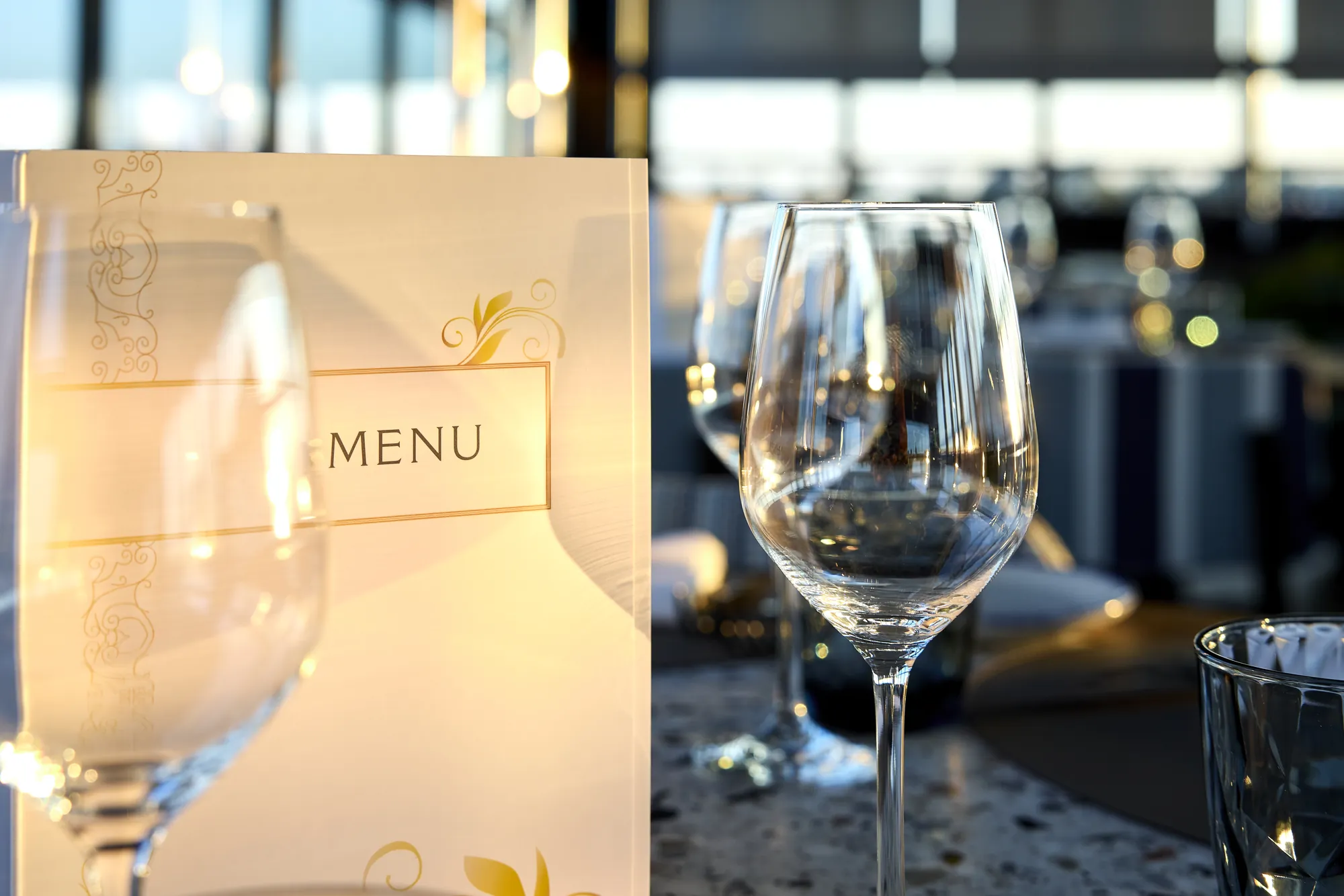 Elegantes Restaurant Menü mit Weingläsern im Hintergrund.