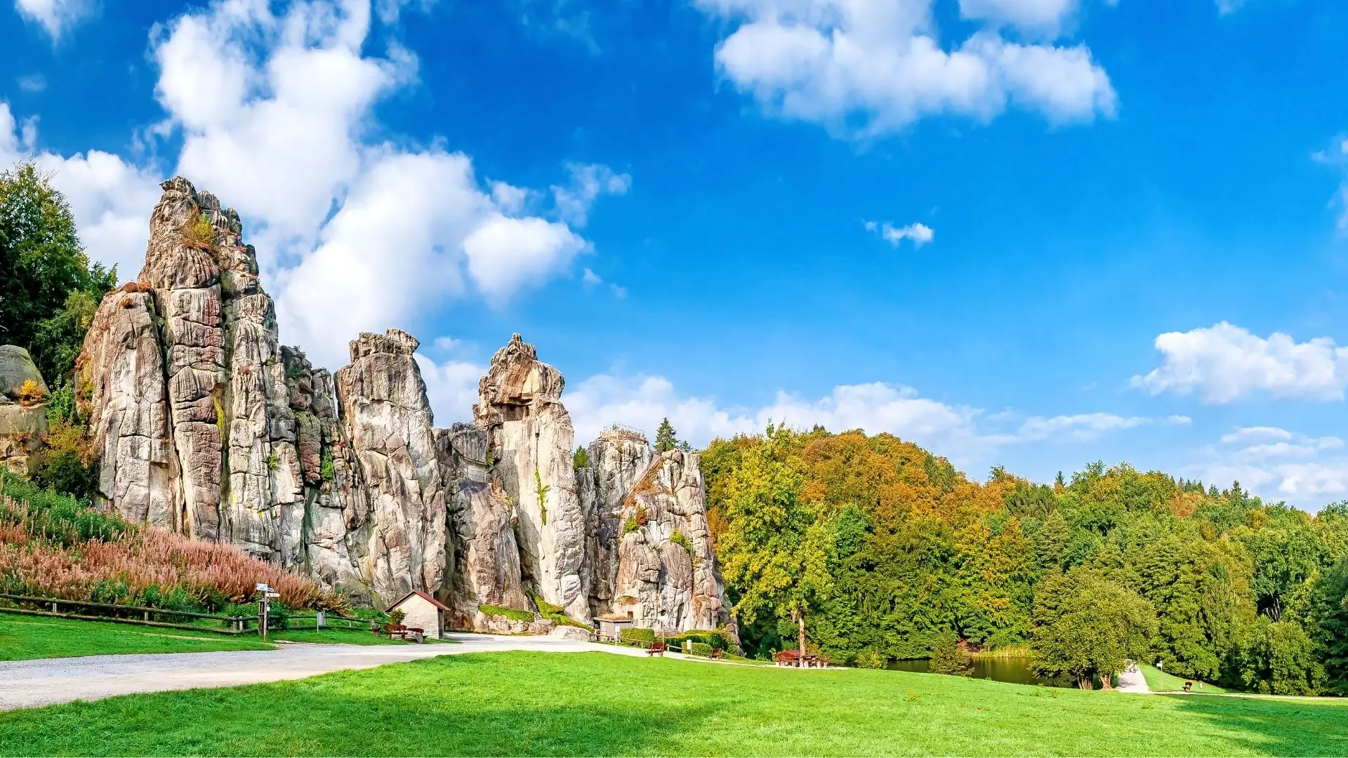 Felsformation Externsteine mit steilen, hohen Sandsteinfelsen vor bewaldetem Hügel und blauem Himmel