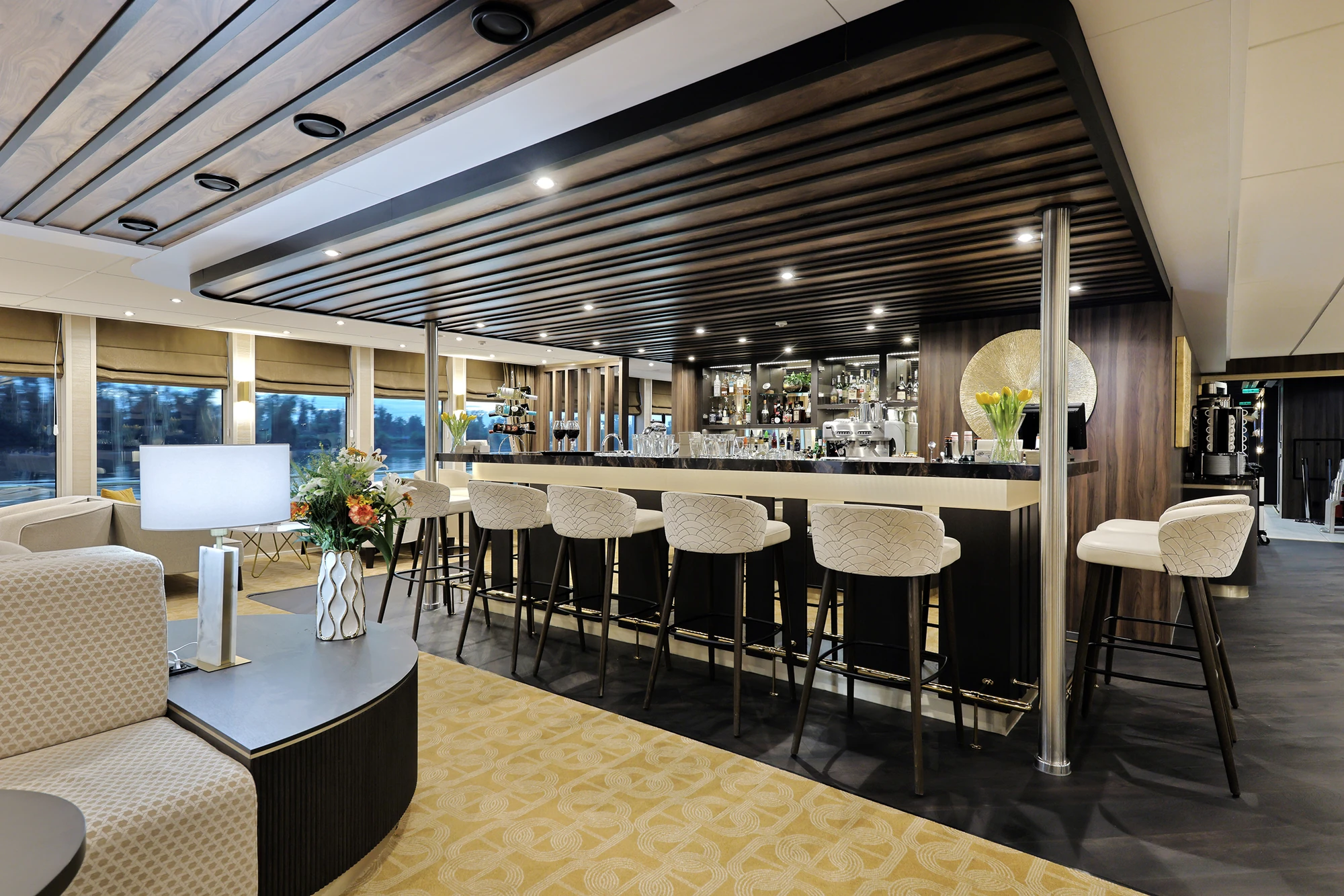 Moderne Bar mit langem Tresen, hohen Hockern und gemütlichen Sitzbereichen in einem hellen, eleganten Raum